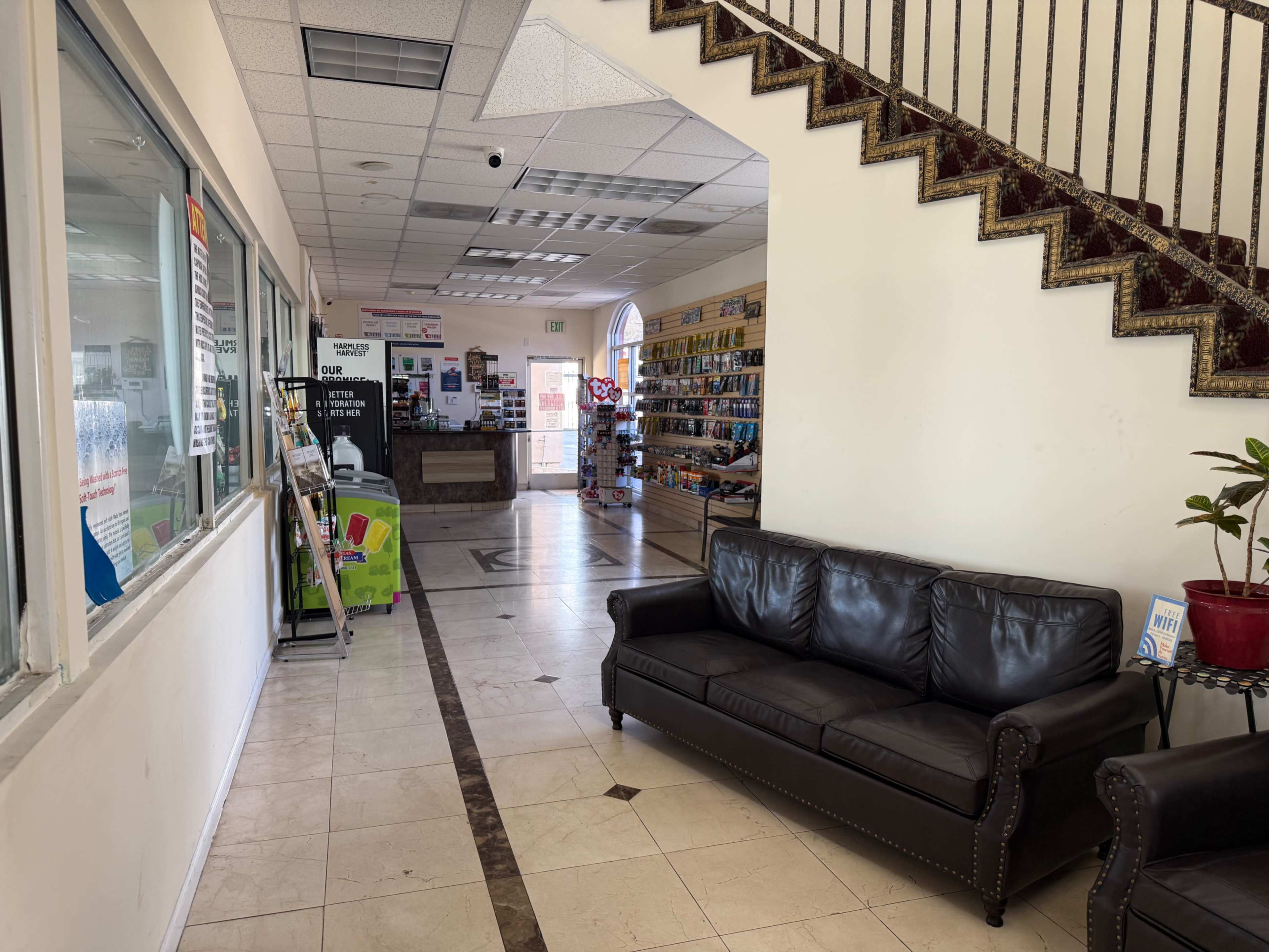 The image shows a spacious interior of a building with a leather sofa on the left, a staircase in the back, and various shelves and a counter visible in the distance.