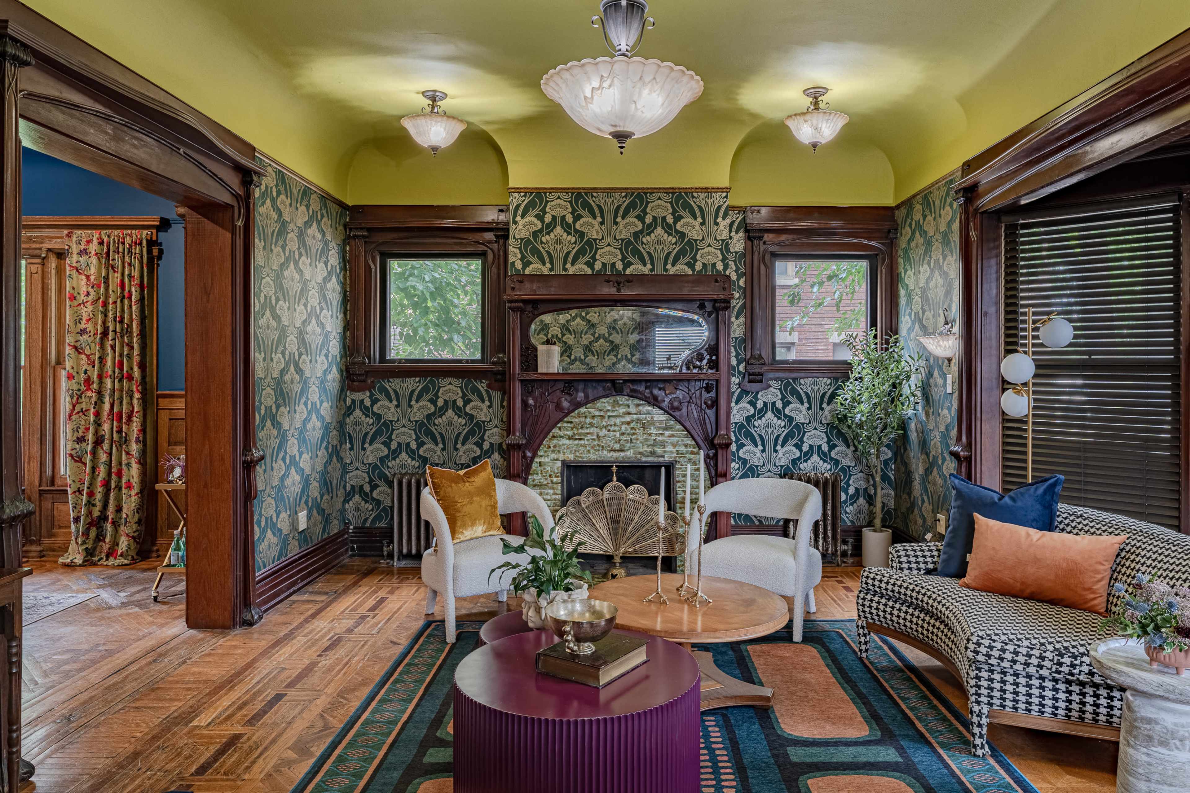 A cozy living room with patterned wallpaper, a decorative fireplace, and a seating area featuring a round coffee table and various plants.