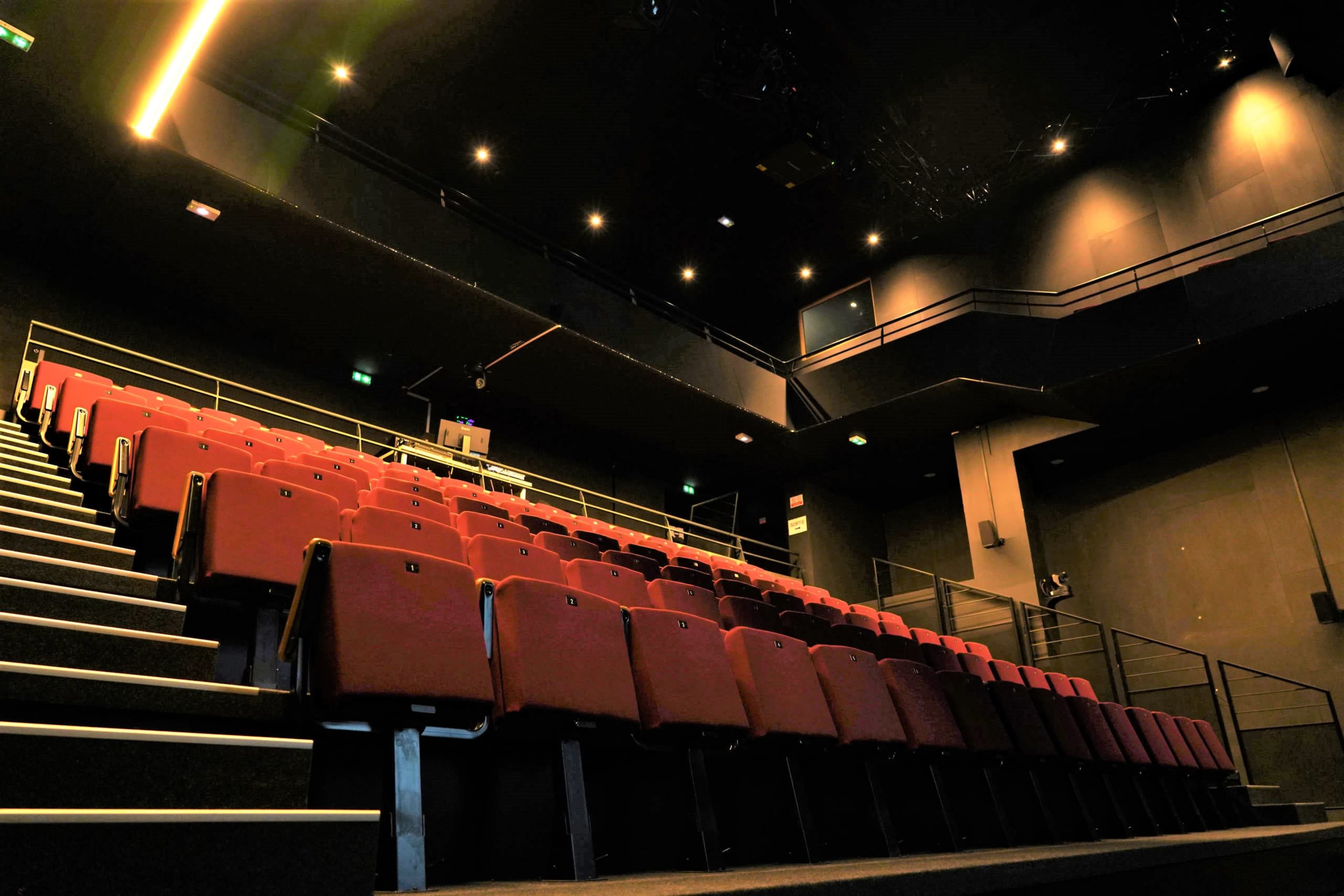 A dimly lit theater with red seating arranged in ascending rows.