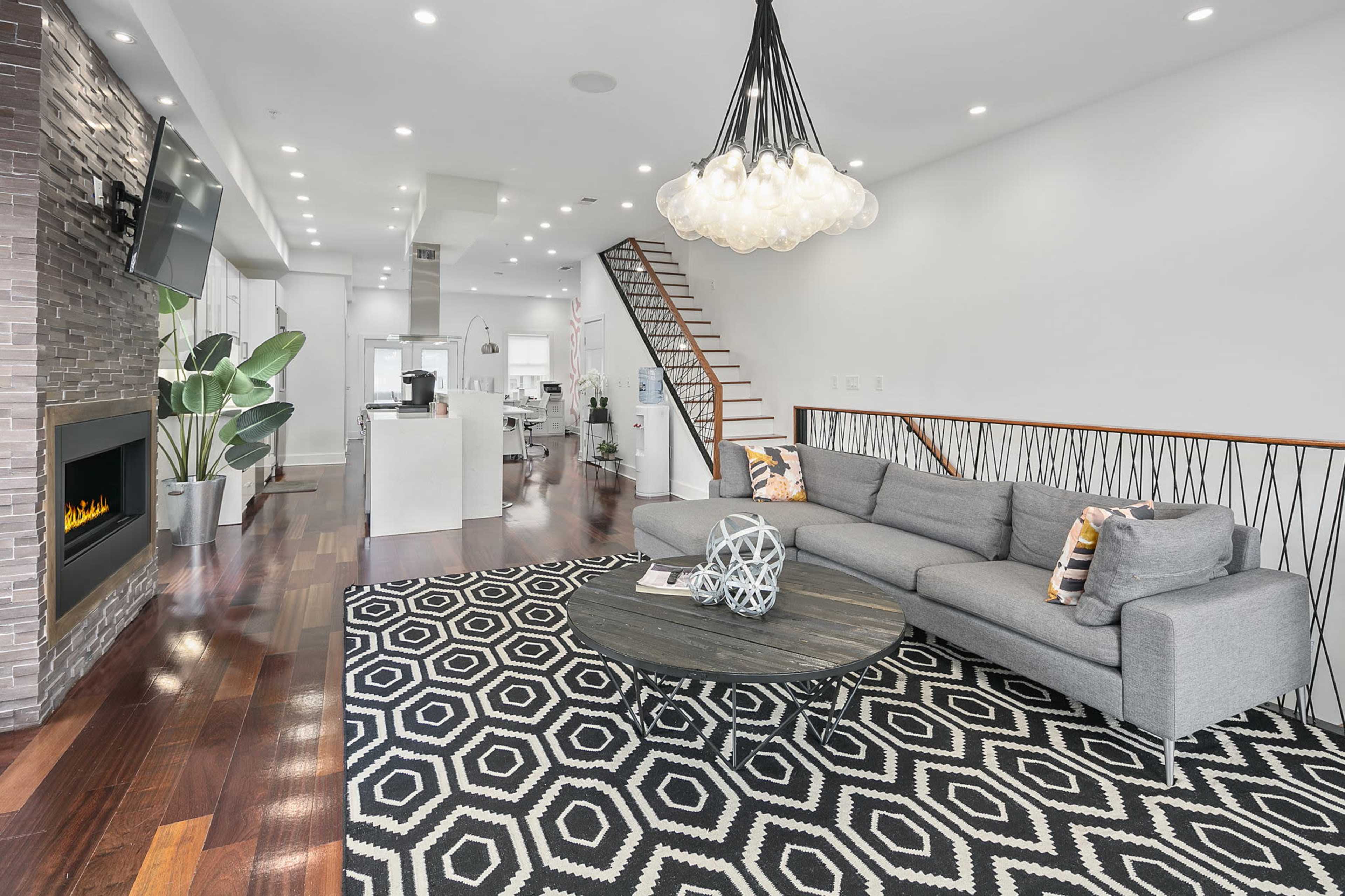 A modern living room featuring a gray sectional sofa, a round coffee table, a patterned rug, and a staircase leading to an upper level.