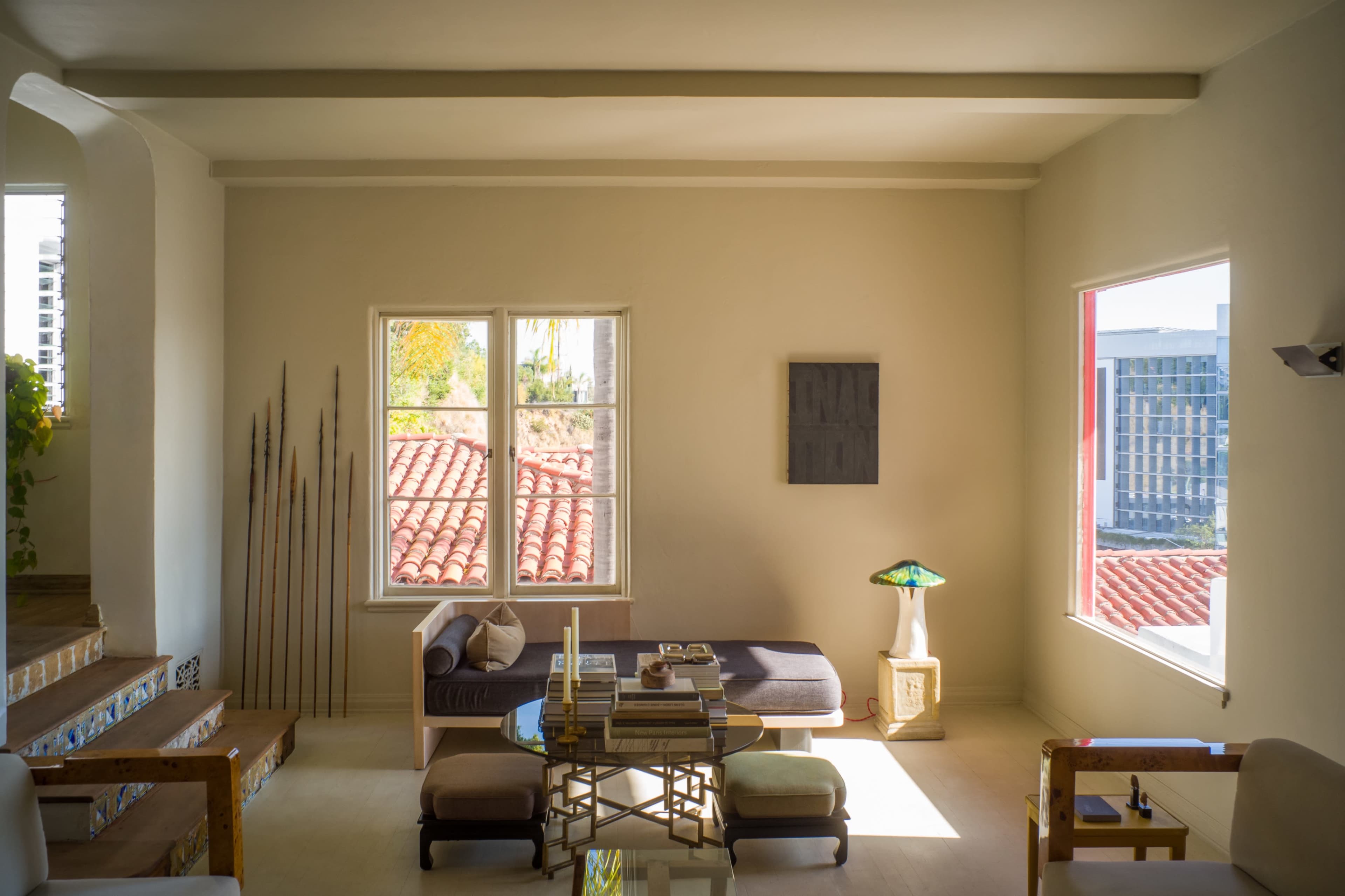 A modern living room features a sofa, coffee table, and large windows with views of a tiled roof and cityscape.