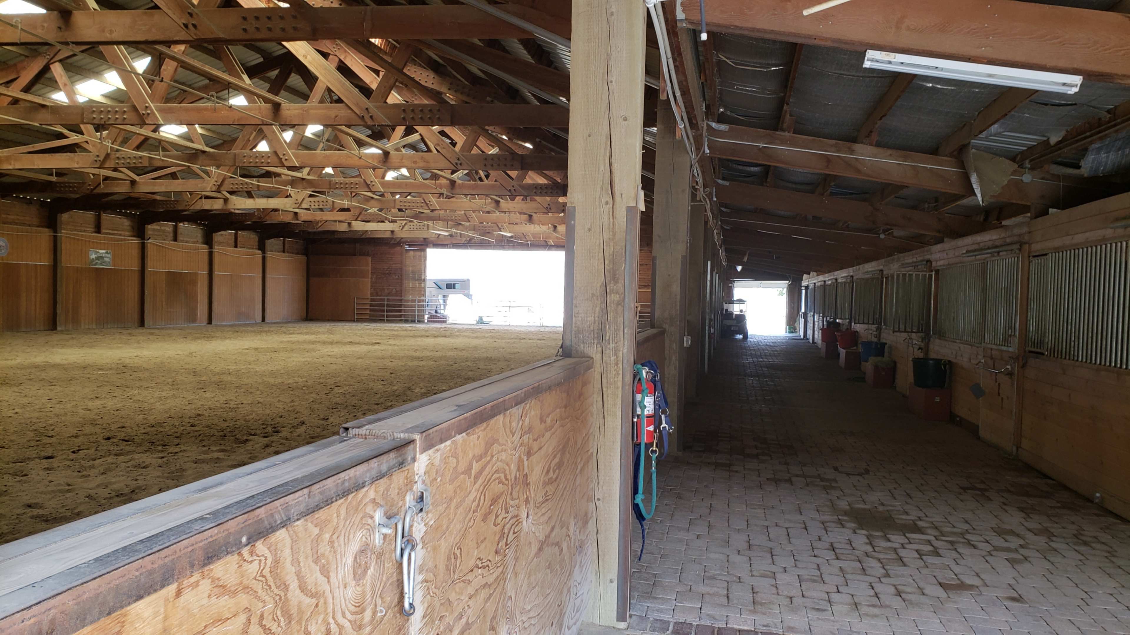 The interior of a large barn with an empty riding arena on the left and a row of horse stalls on the right.
