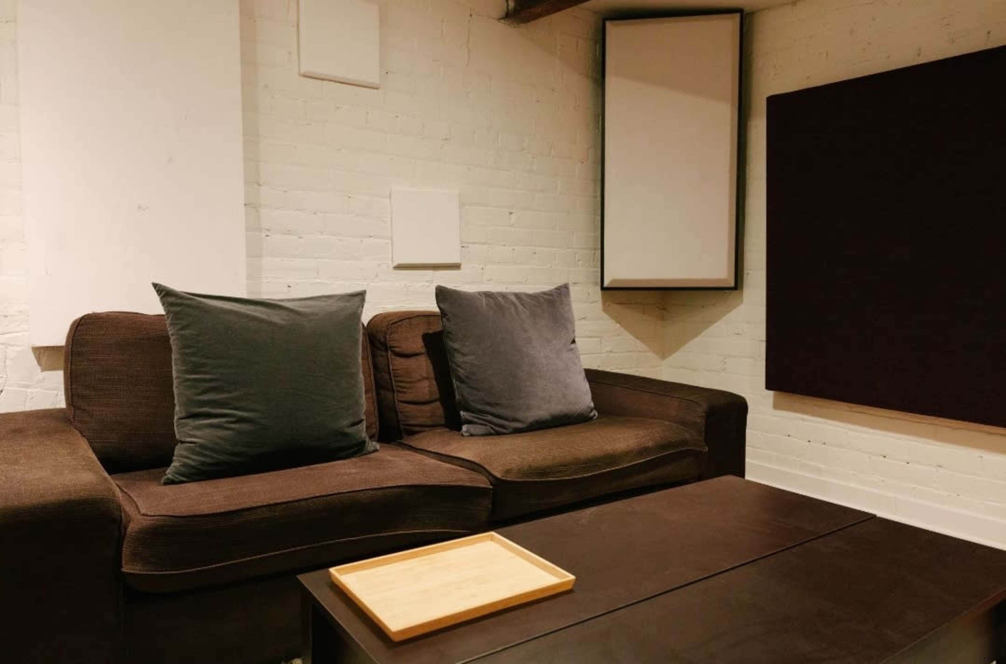 The image shows a cozy living space with a brown sofa and a wooden coffee table, set against a white brick wall.