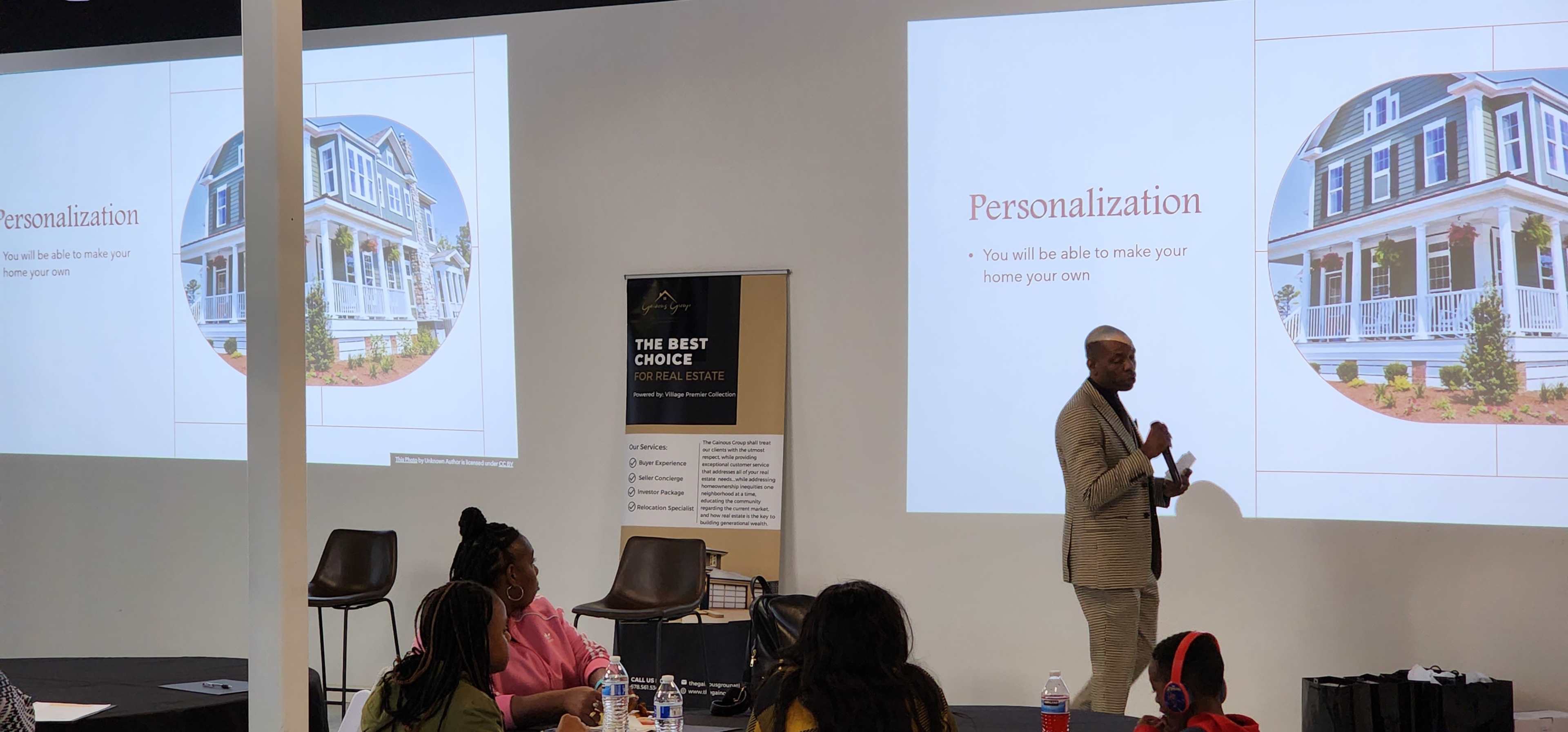 A speaker presents on personalization in home design to an audience seated in a seminar space with a large projection screen.