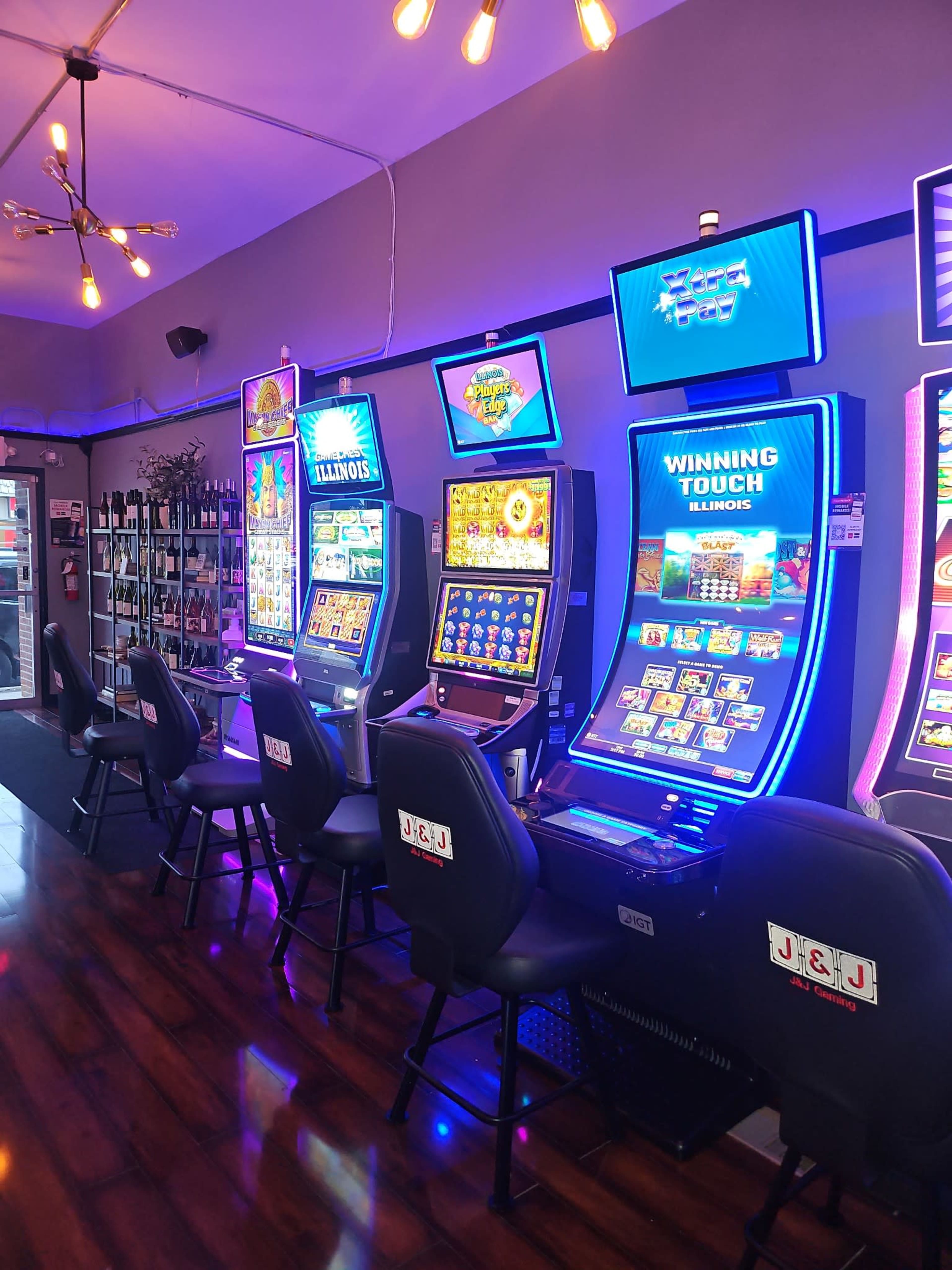 The image shows a row of illuminated slot machines inside a gaming establishment, with a counter and various gaming displays visible in the background.