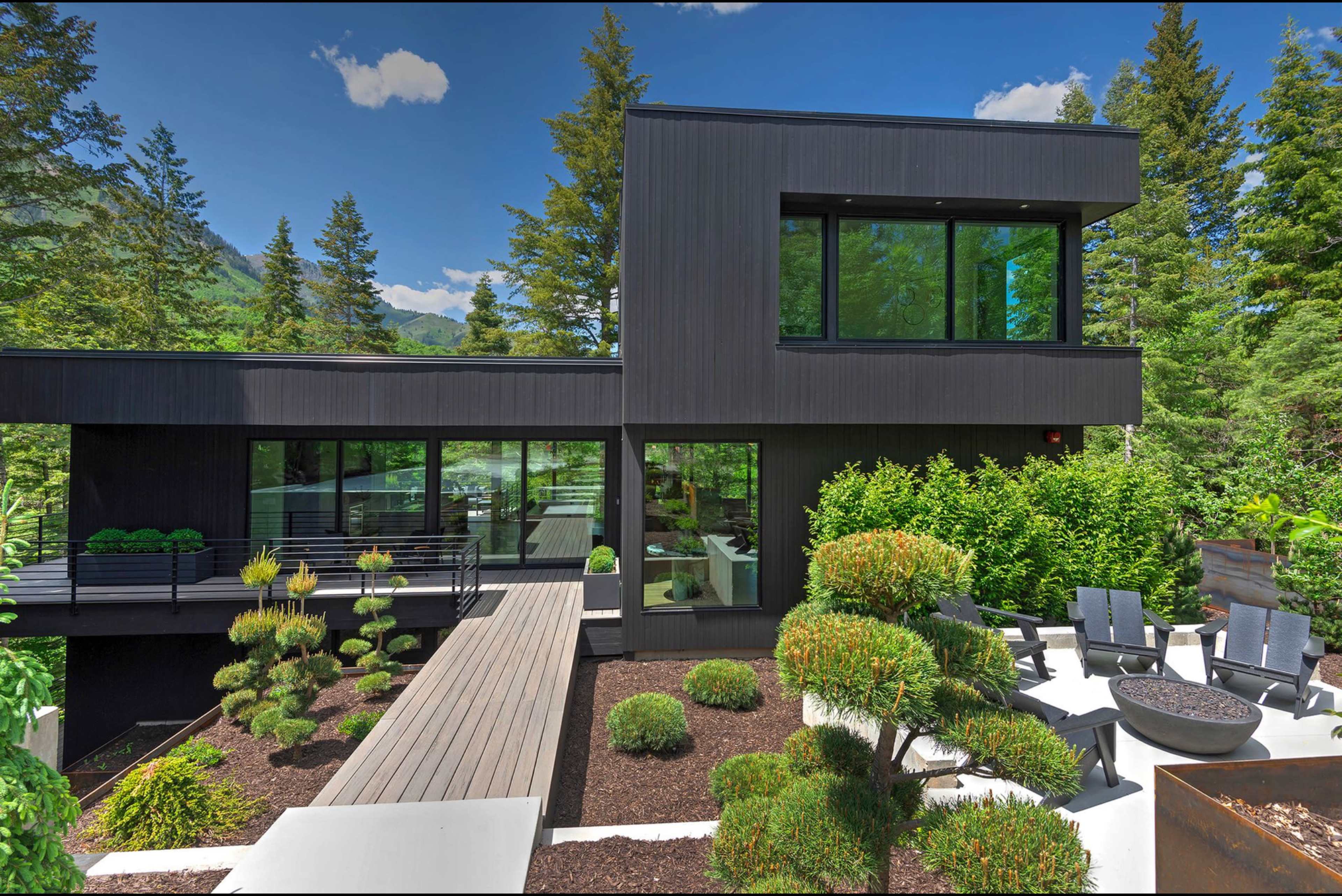 The image shows a modern black exterior house surrounded by landscaped gardens and greenery.