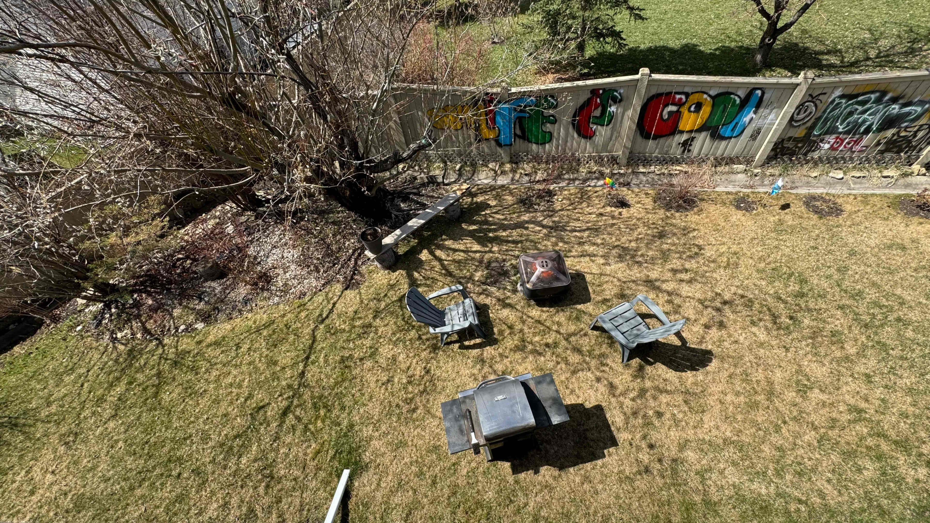 A backyard with a fire pit surrounded by four wooden chairs and a fence decorated with colorful graffiti.
