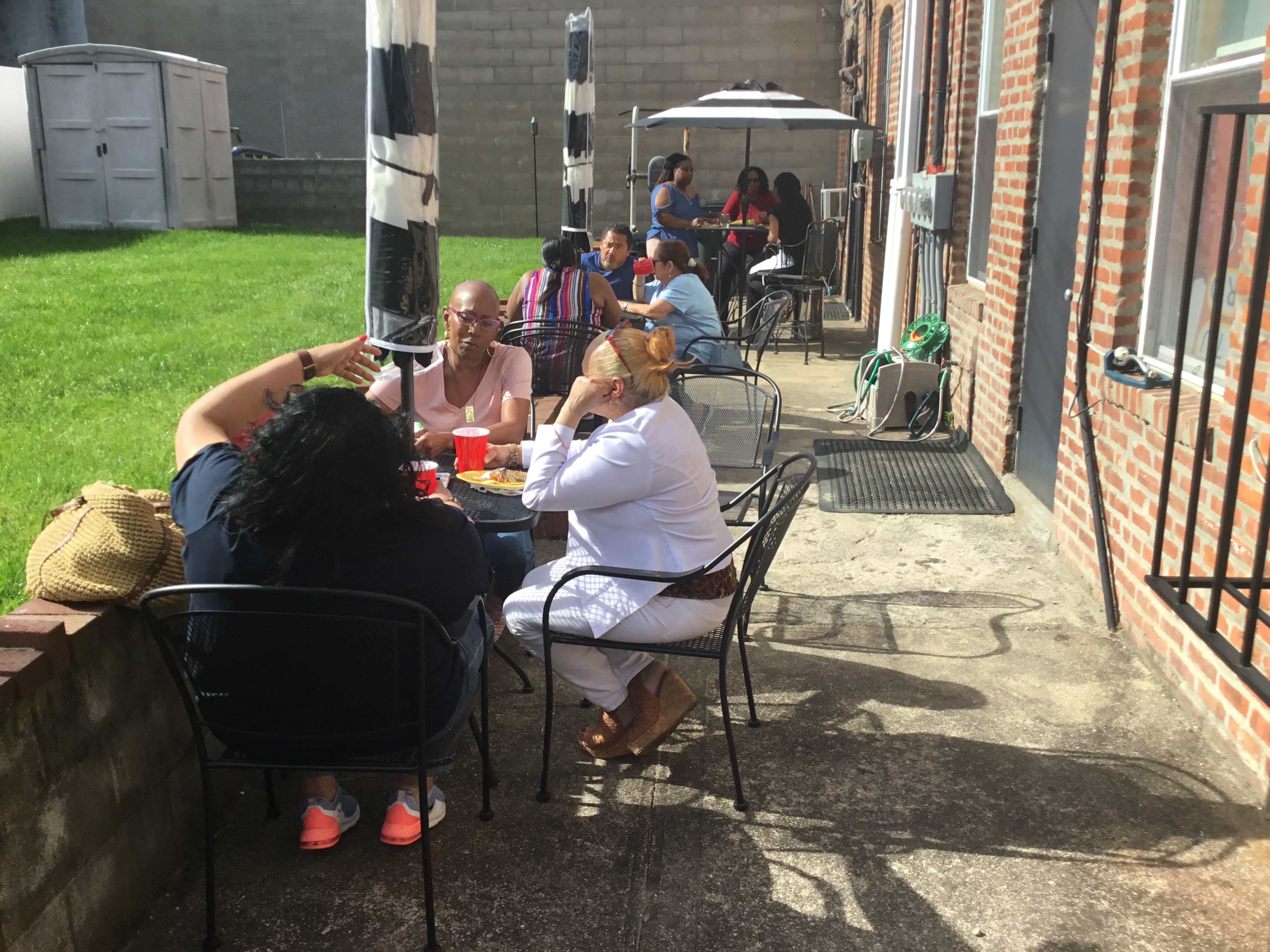 A group of people sits at outdoor tables enjoying food and drinks in a sunny courtyard.