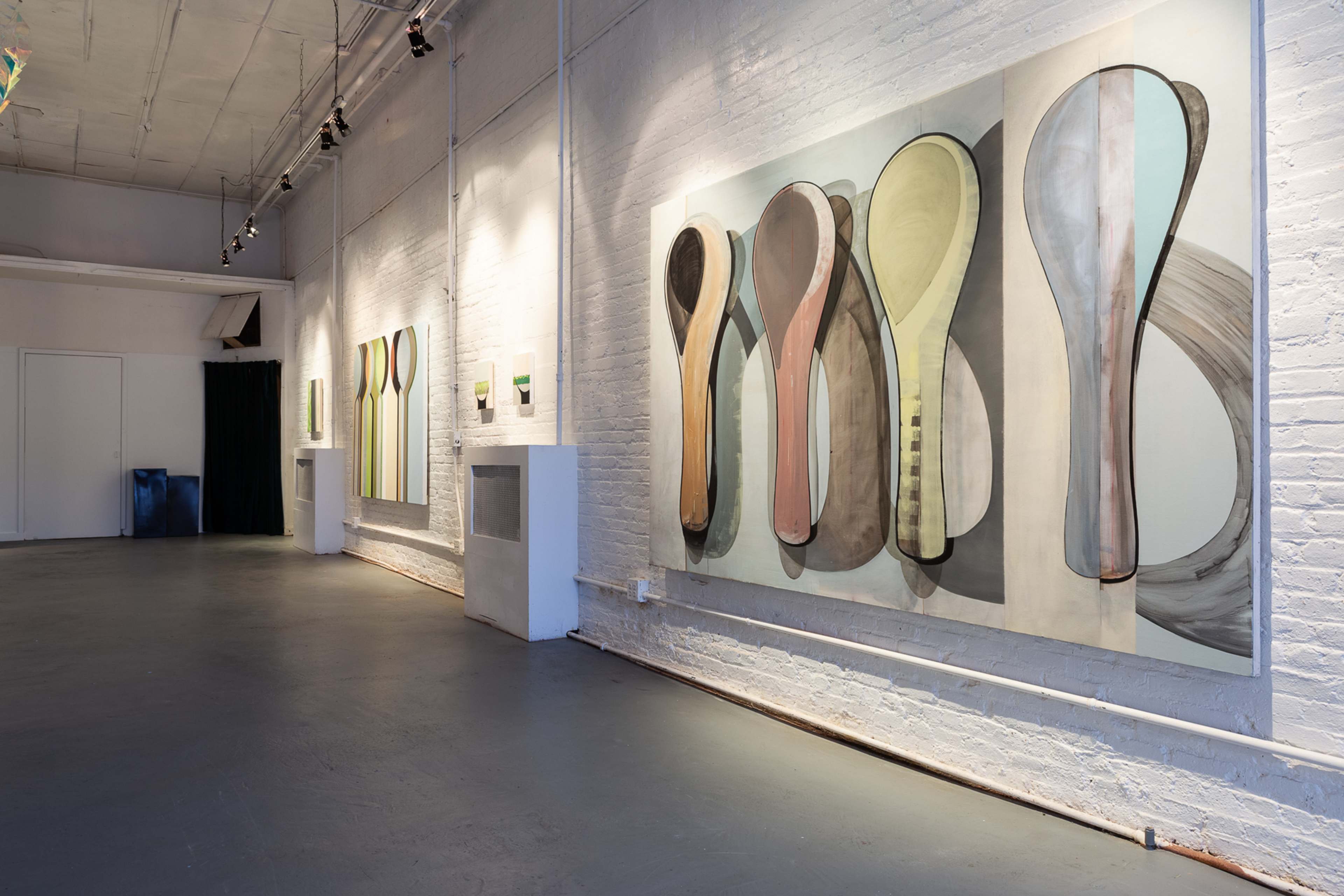 The image shows an art gallery interior with large abstract paintings on the white brick walls and a grey floor.