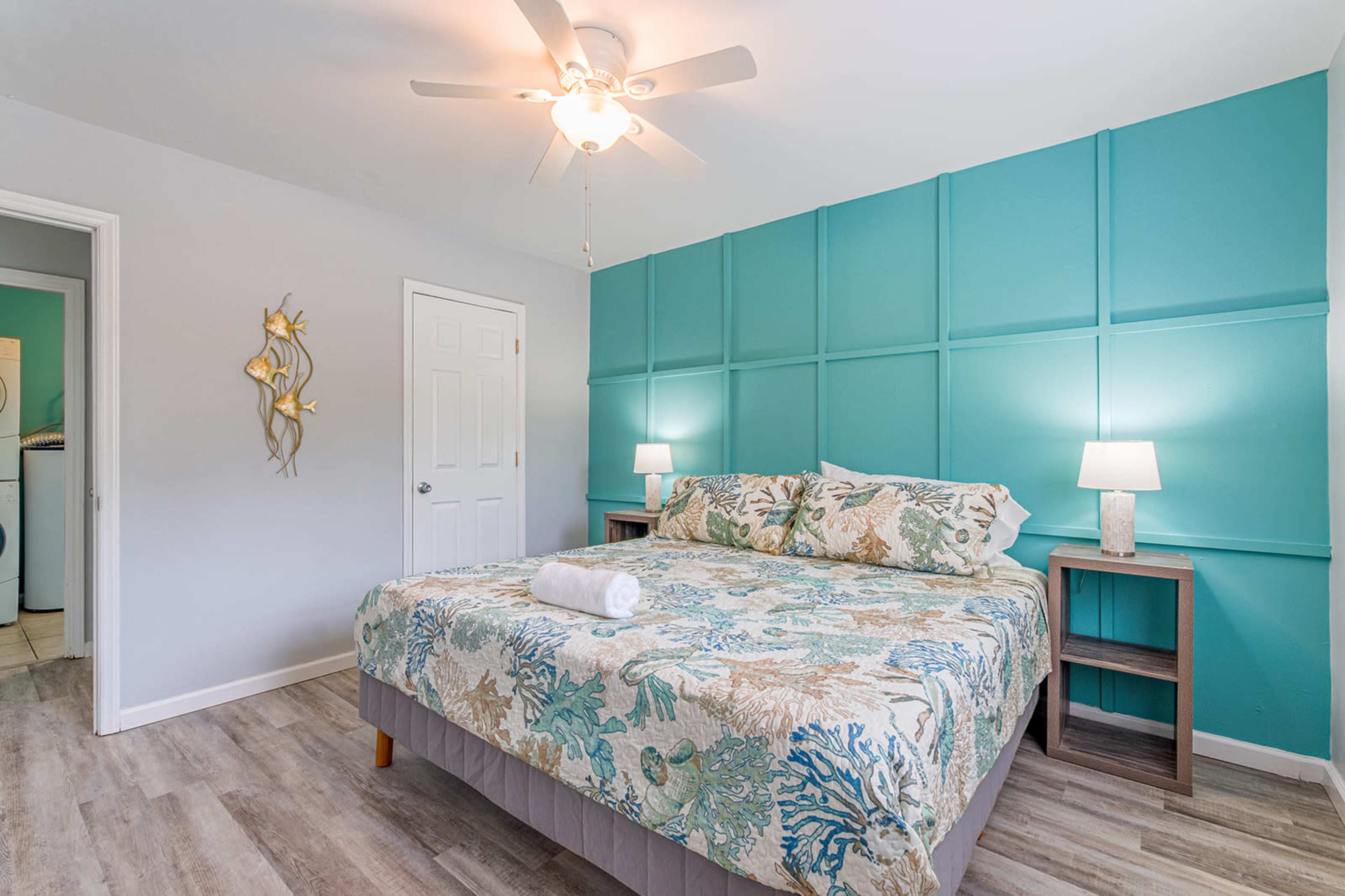 A neatly arranged bedroom features a large bed with a patterned comforter, turquoise accent wall, and two bedside tables with lamps.