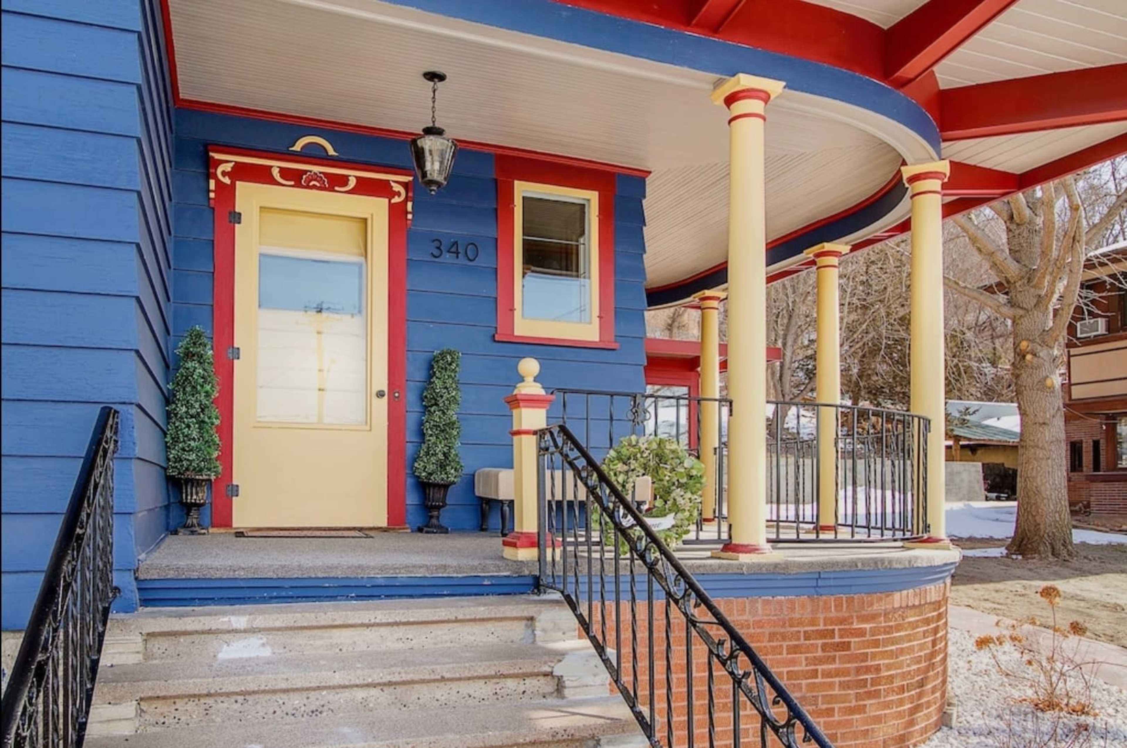 A brightly colored home entrance with blue siding, a yellow door, and decorative red columns, featuring a front porch and steps leading up to it.