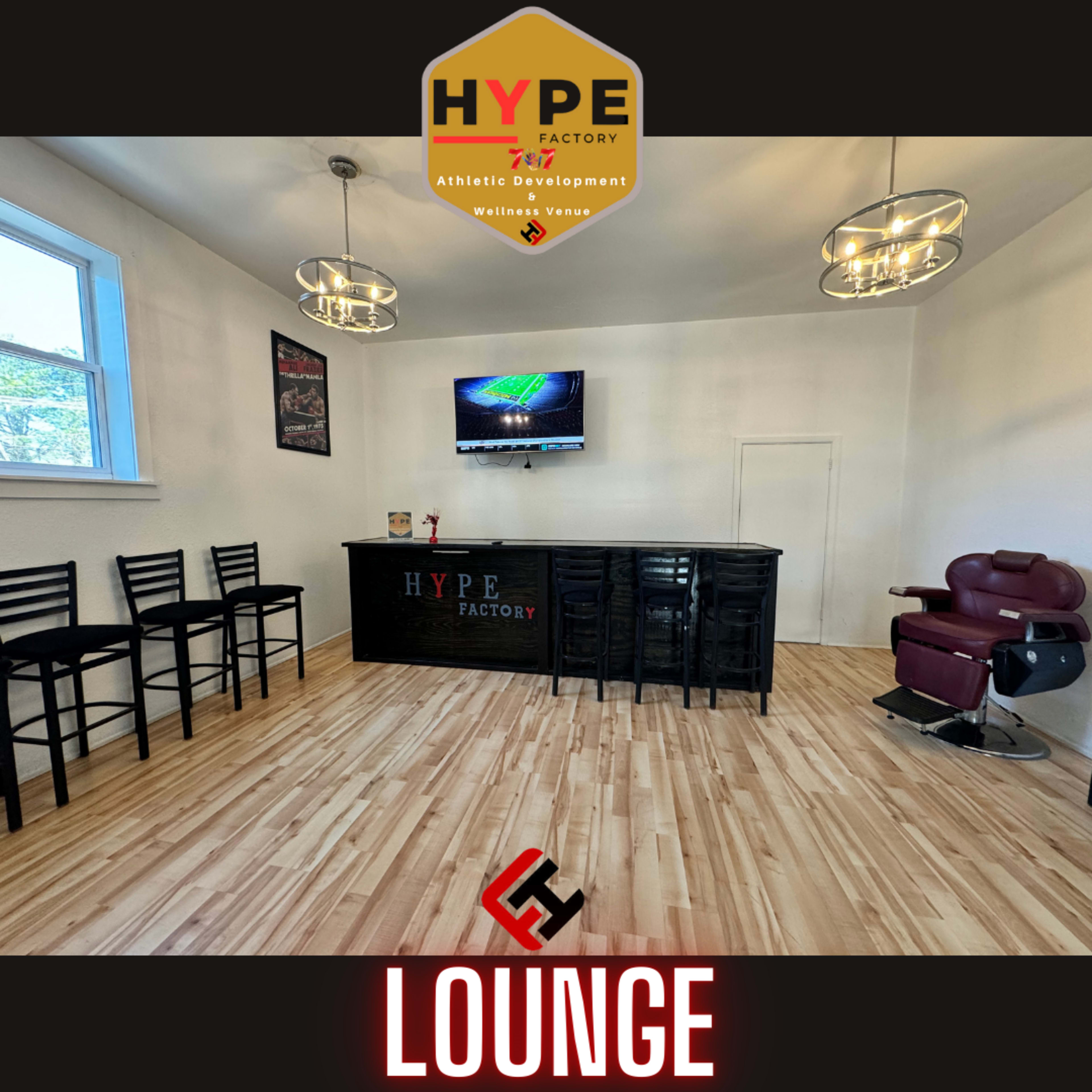 A clean, modern lounge area with a bar counter, seating, and a large screen mounted on the wall.