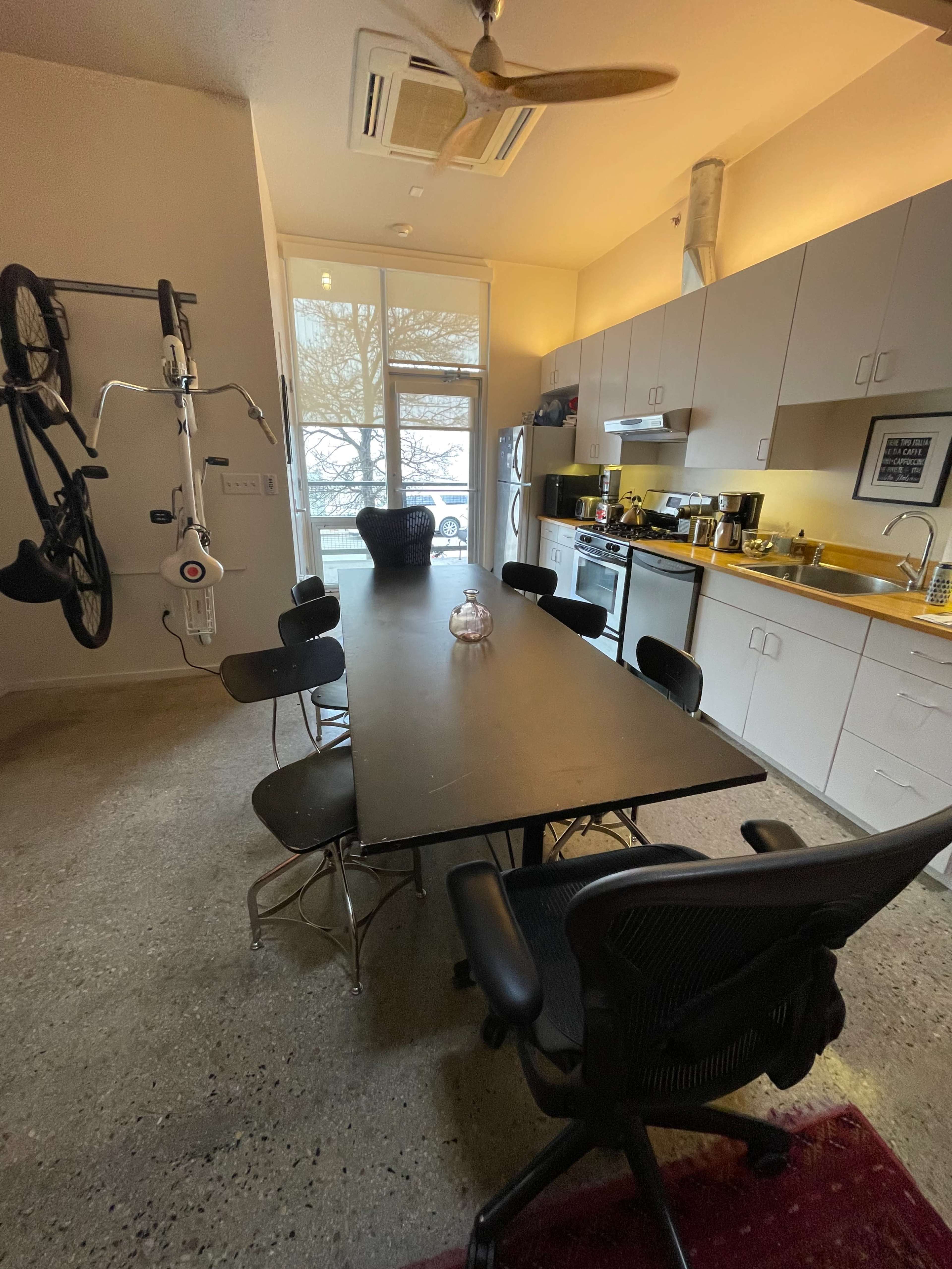 A modern kitchen and dining area with a long table surrounded by chairs and bicycles mounted on the wall.