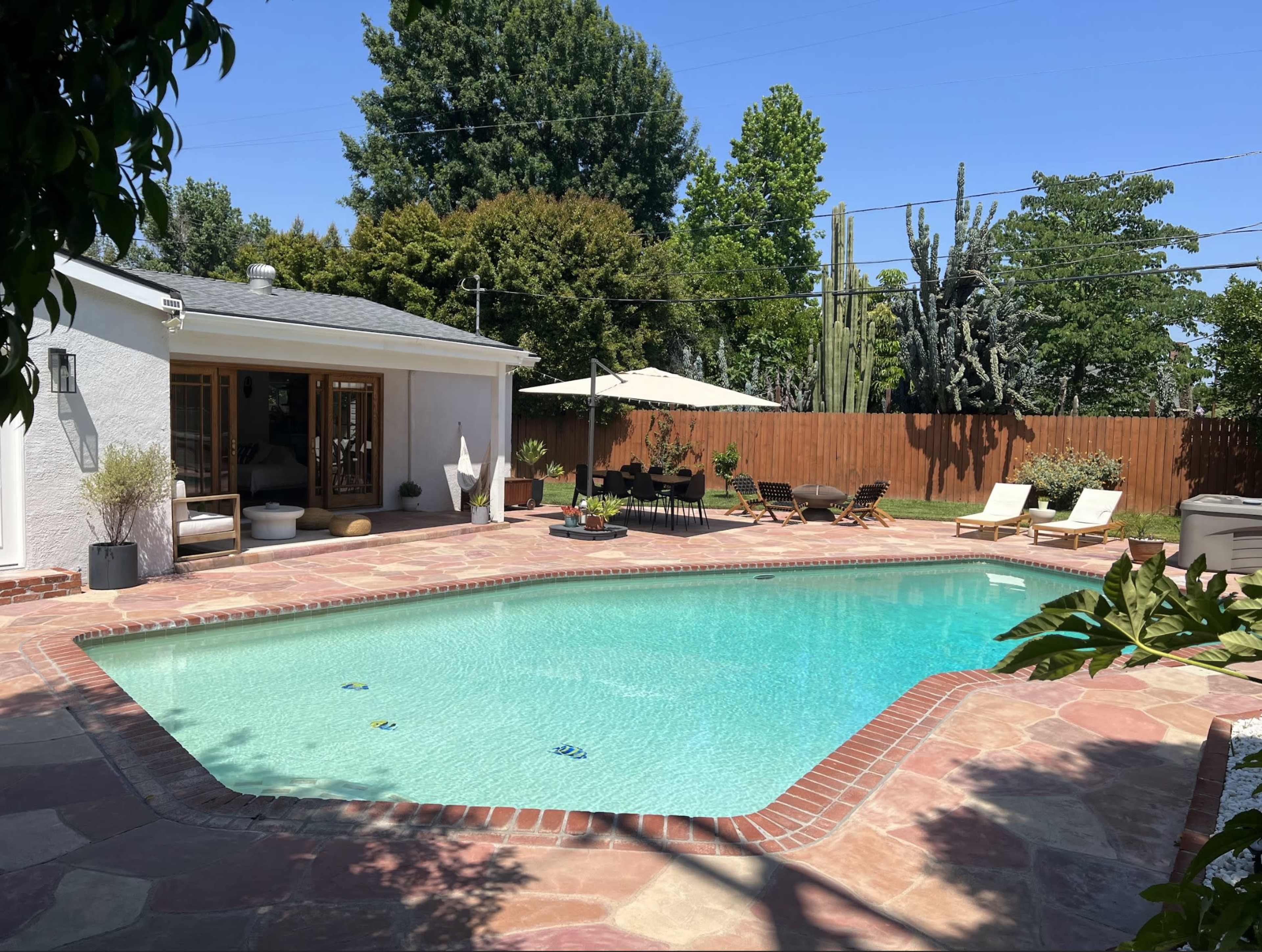 The image shows a backyard with a swimming pool surrounded by lounge chairs and an umbrella, with a housing structure visible in the background.