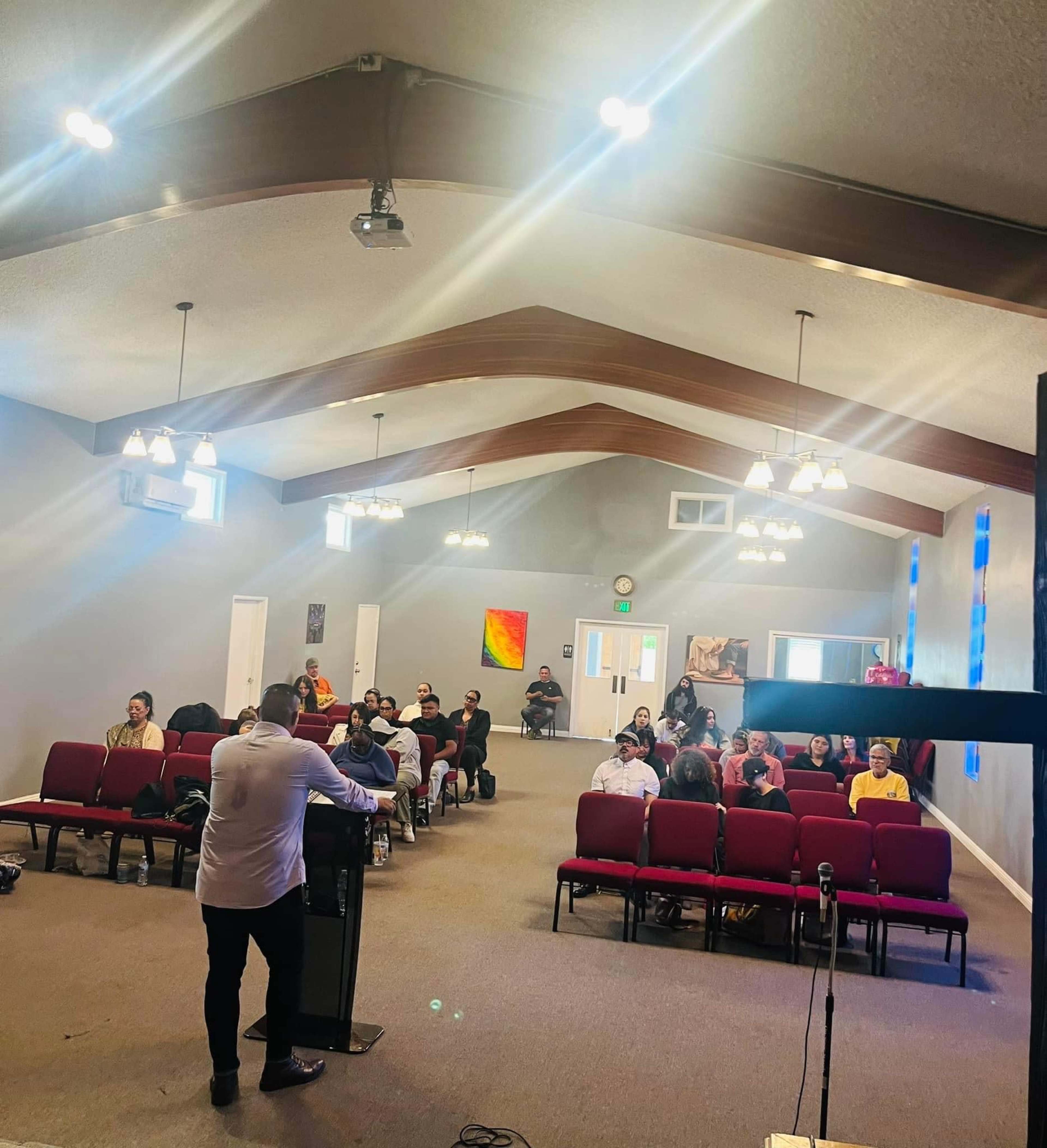 A speaker stands at a podium while an audience faces them in a well-lit church interior.