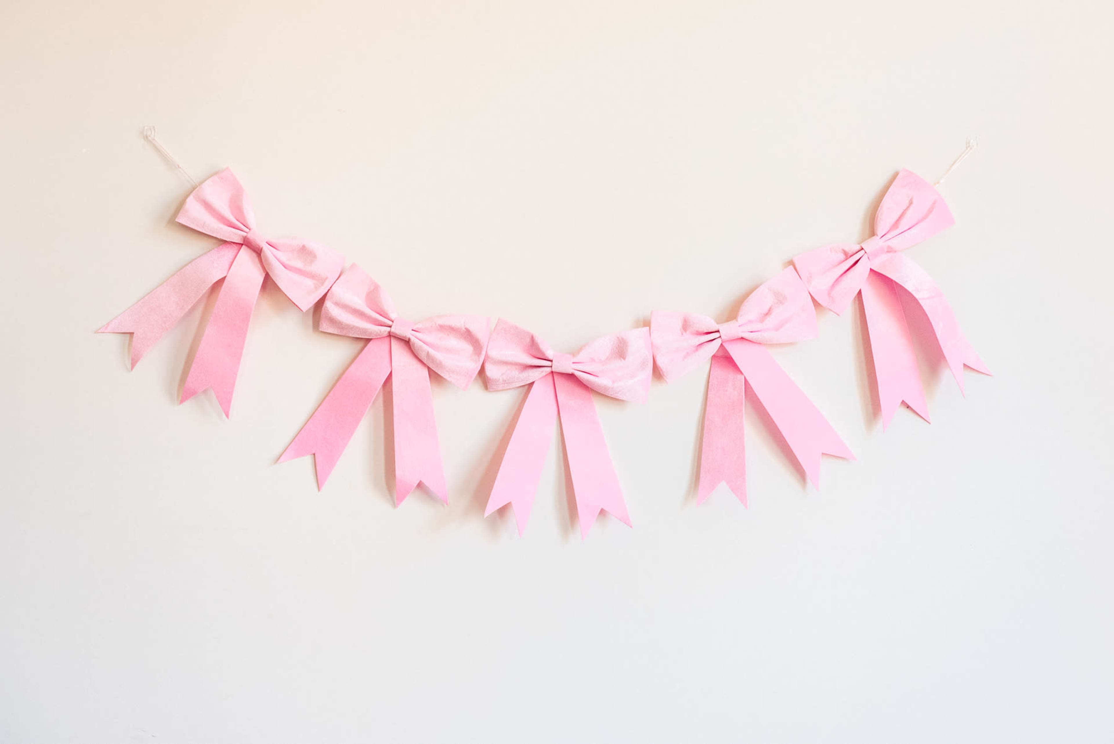 A garland made of pink ribbons is hung against a white wall.