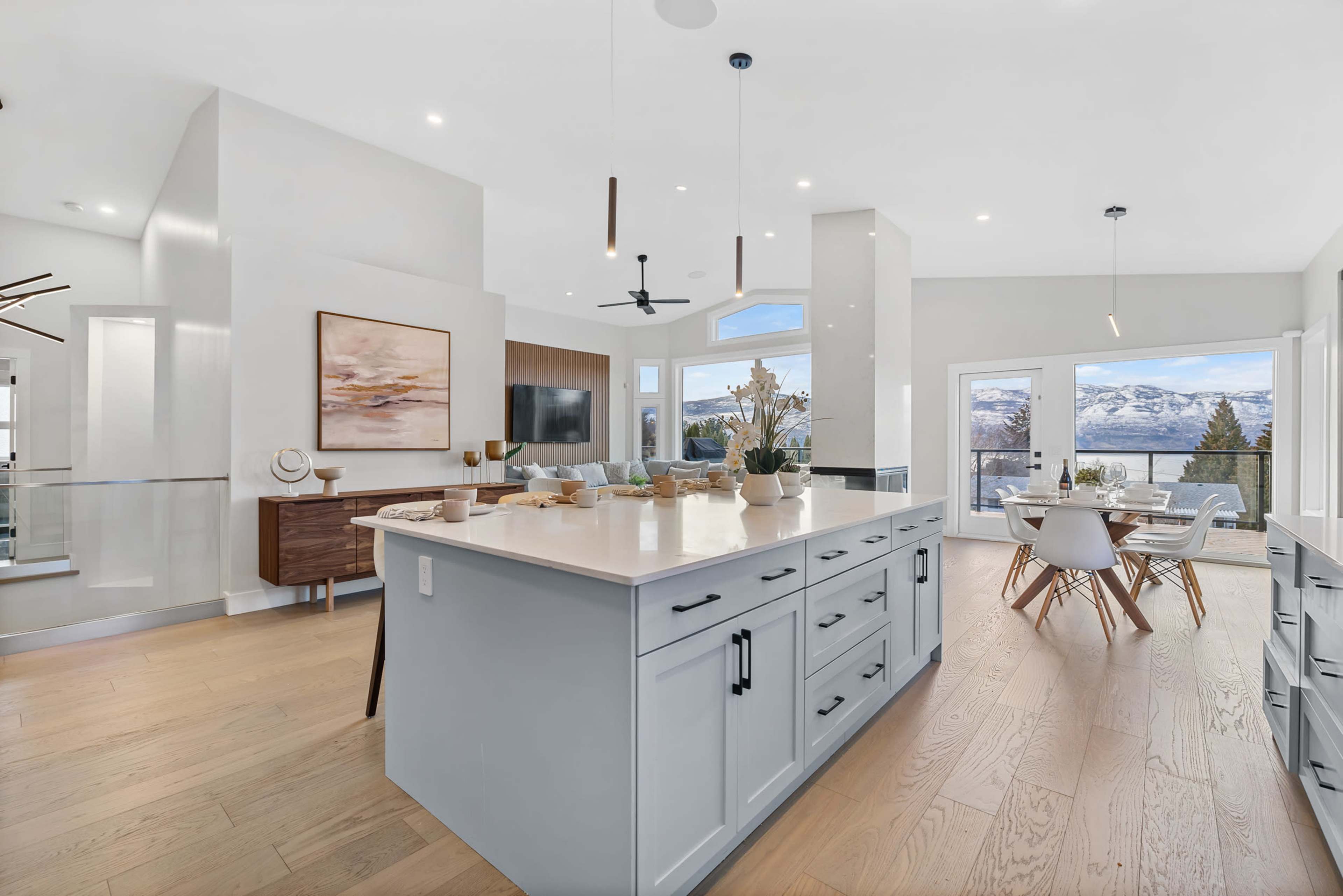 A modern kitchen with a large island, light blue cabinetry, and an open layout that connects to a dining area with panoramic views of the mountains.