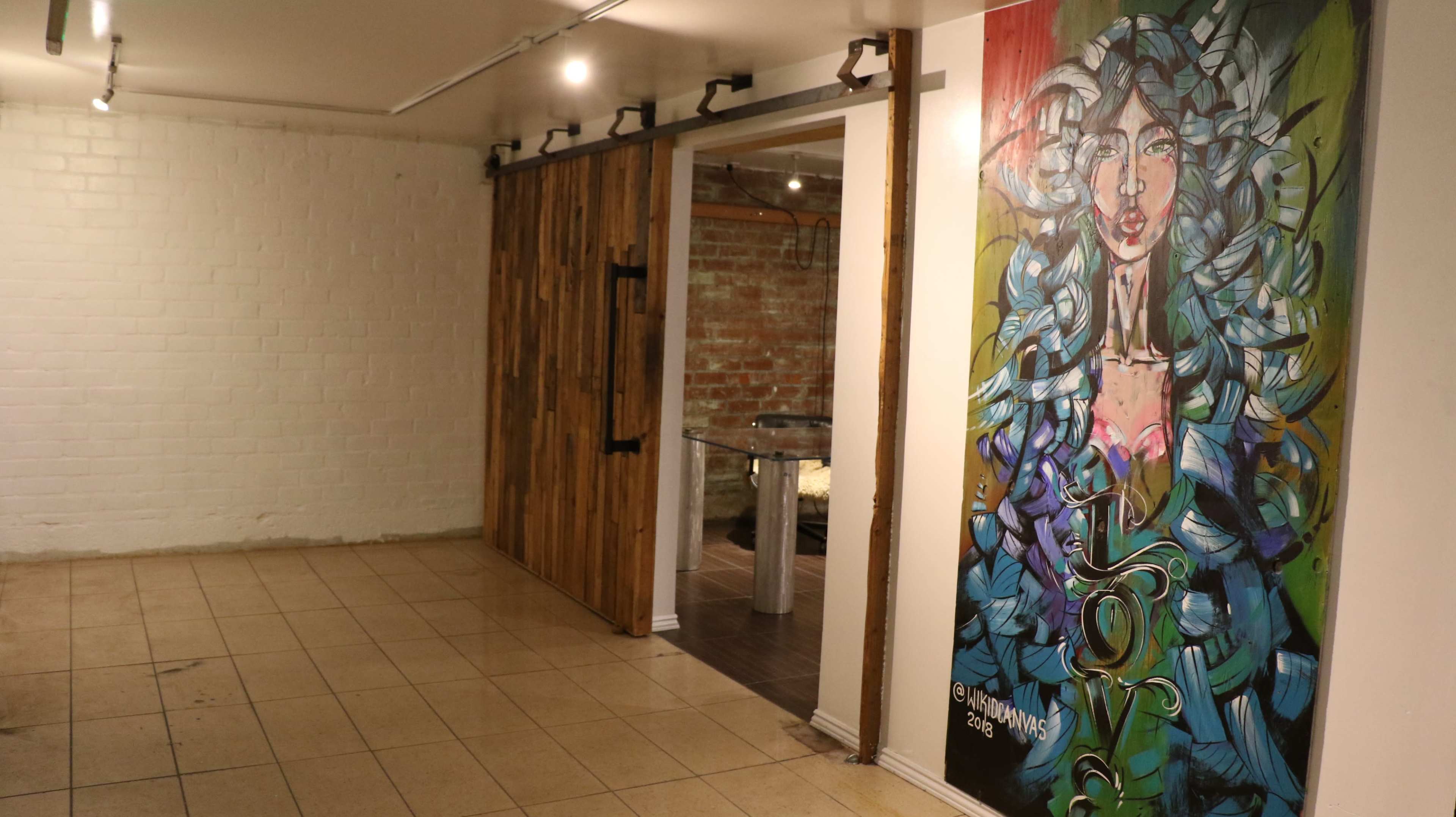 The image shows a spacious room with a tiled floor, a wooden sliding door, and a large colorful mural of a woman on one wall.