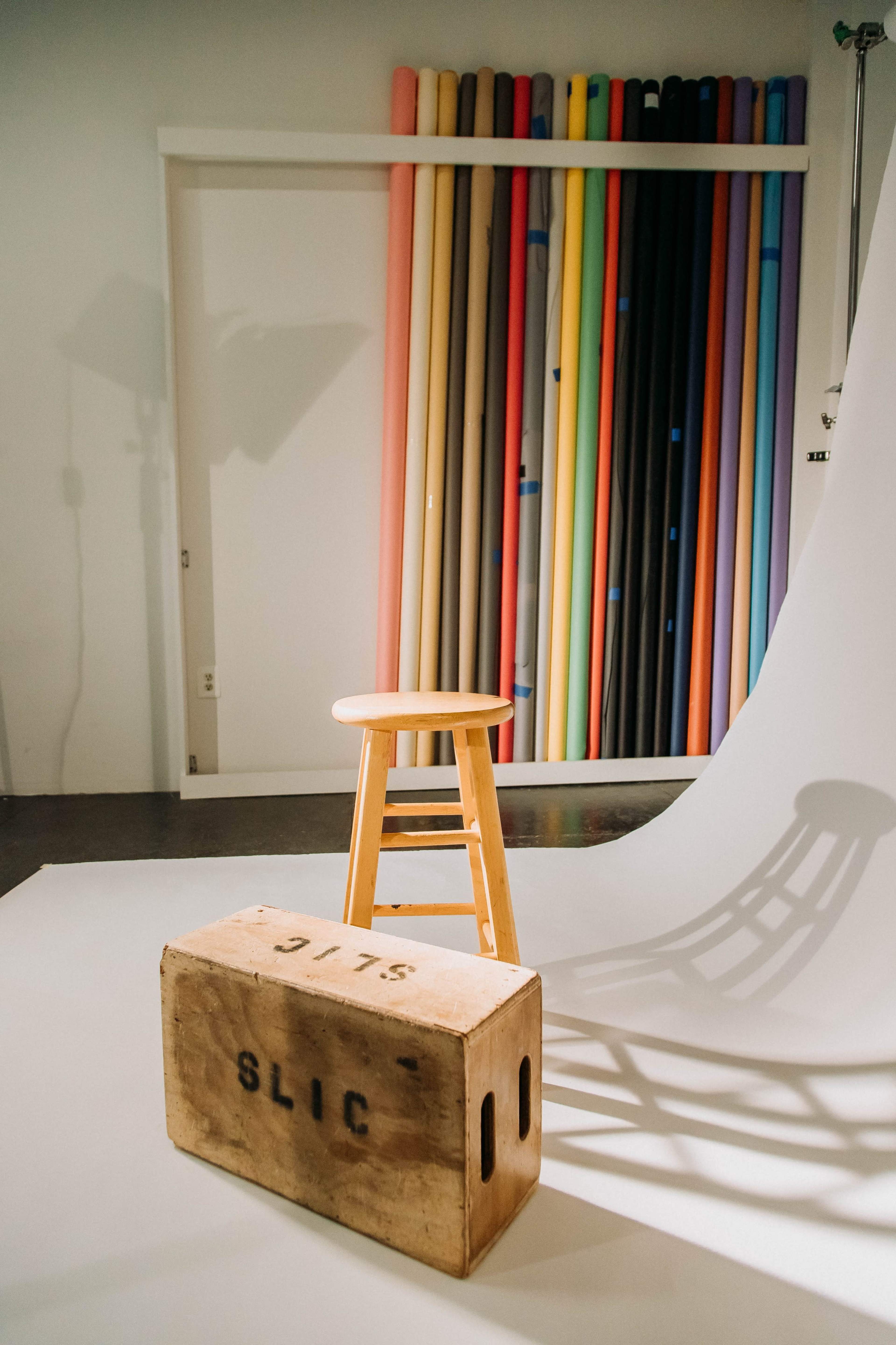 A wooden stool and a box labeled "SLIC" positioned in front of a backdrop of colorful rolled paper.