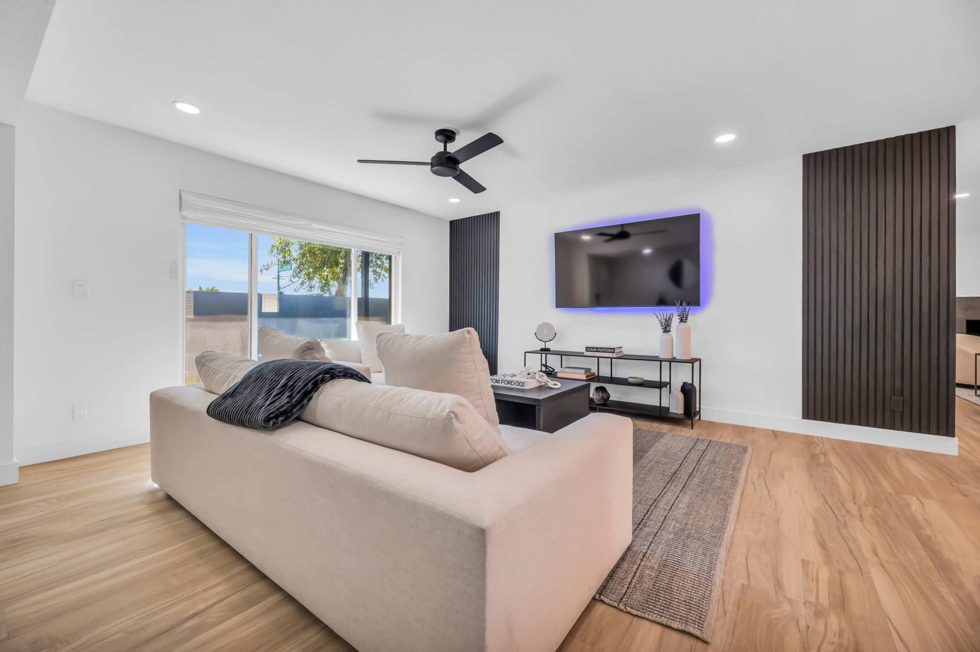 A modern living room features a light-colored sofa, a coffee table, and a wall-mounted television against a backdrop of wood paneling.