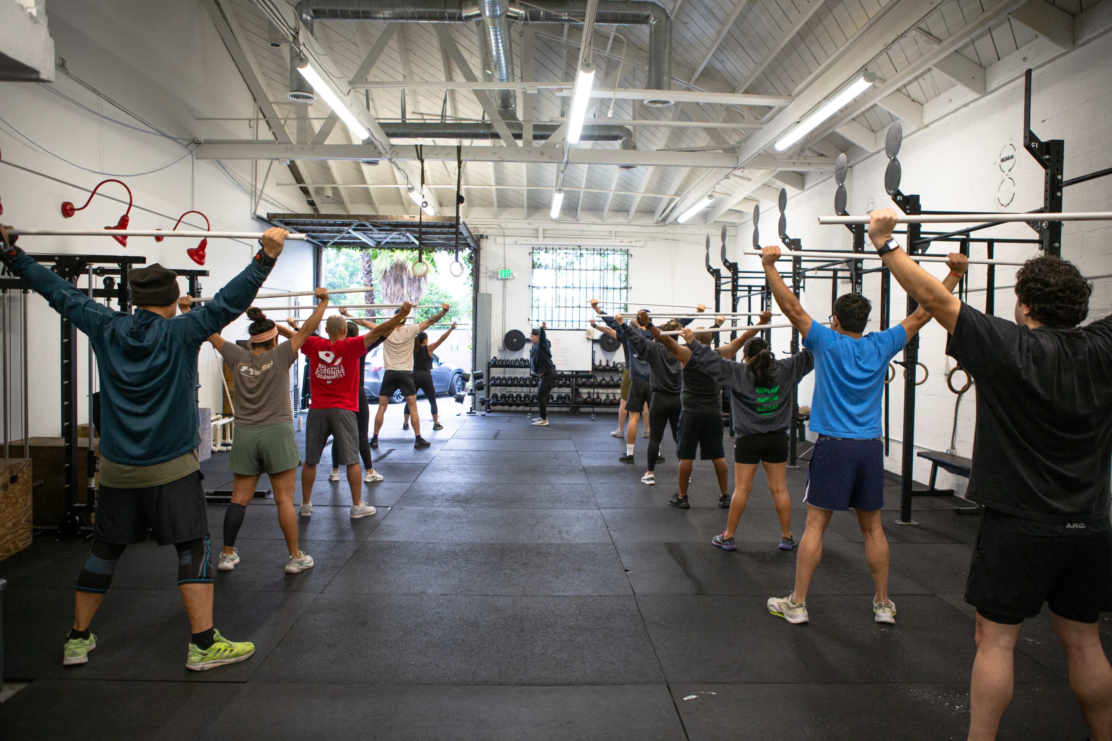 A group of people is engaged in a fitness class, performing overhead exercises with resistance bands in a gym setting.