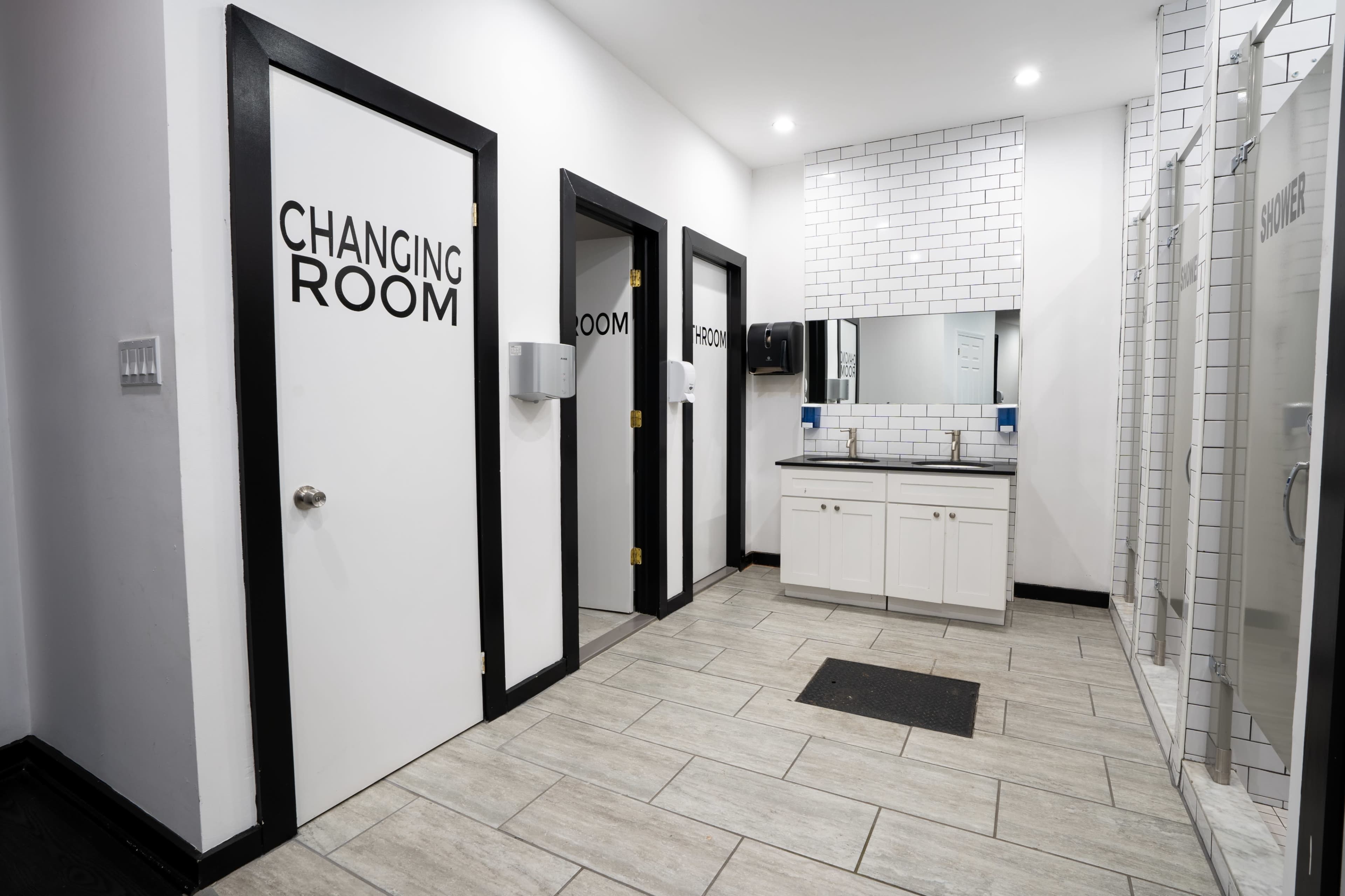 A restroom area featuring three doors labeled "CHANGING ROOM" and "SHOWER," with a sink and mirror along one wall.
