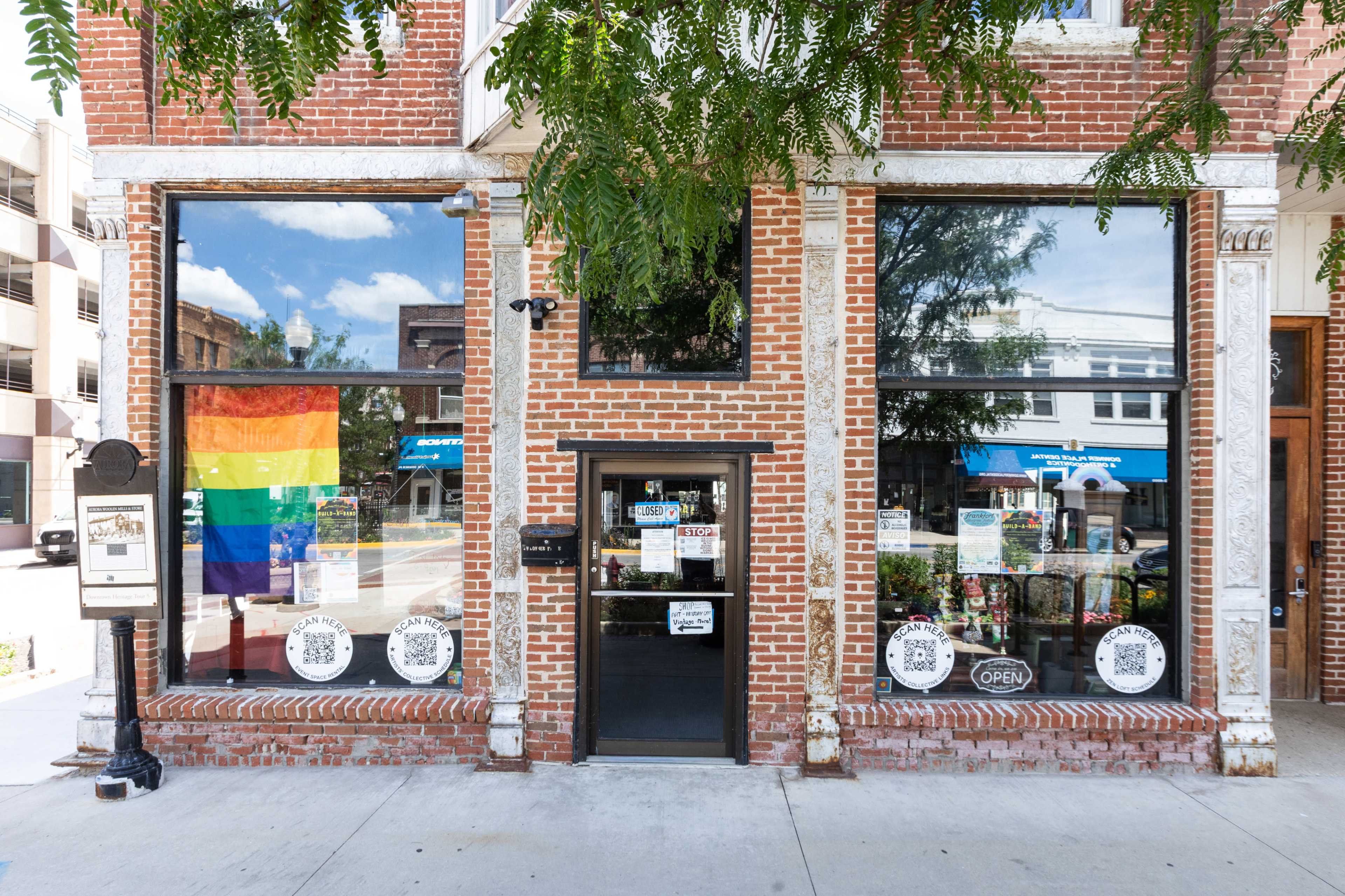 The storefront features large windows displaying a rainbow flag and various signs, with a visible "OPEN" sign and a menu display beside the entrance.