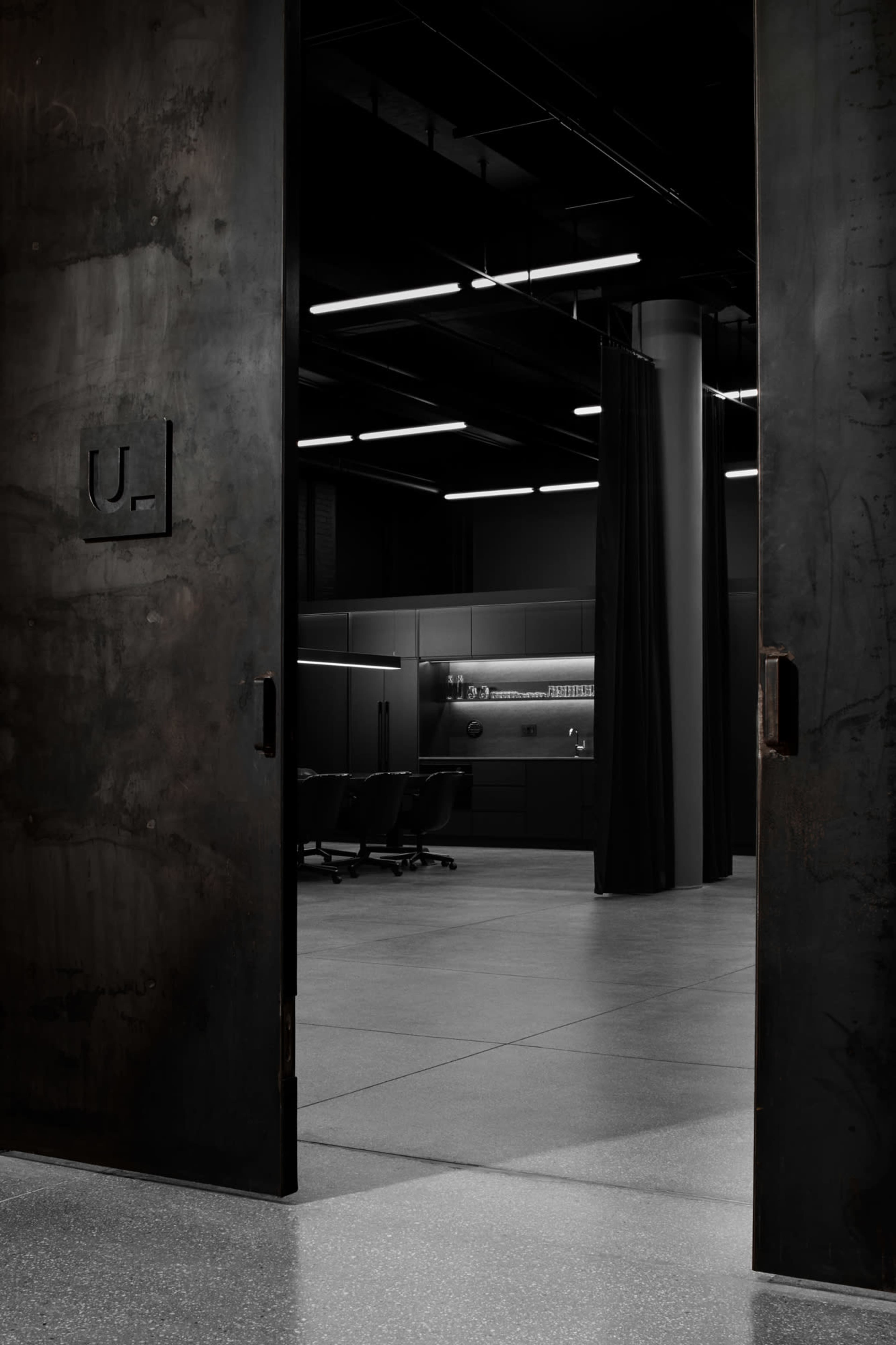 The image shows a dimly lit, modern room with a sleek, industrial design, viewed through a partially opened metal door.