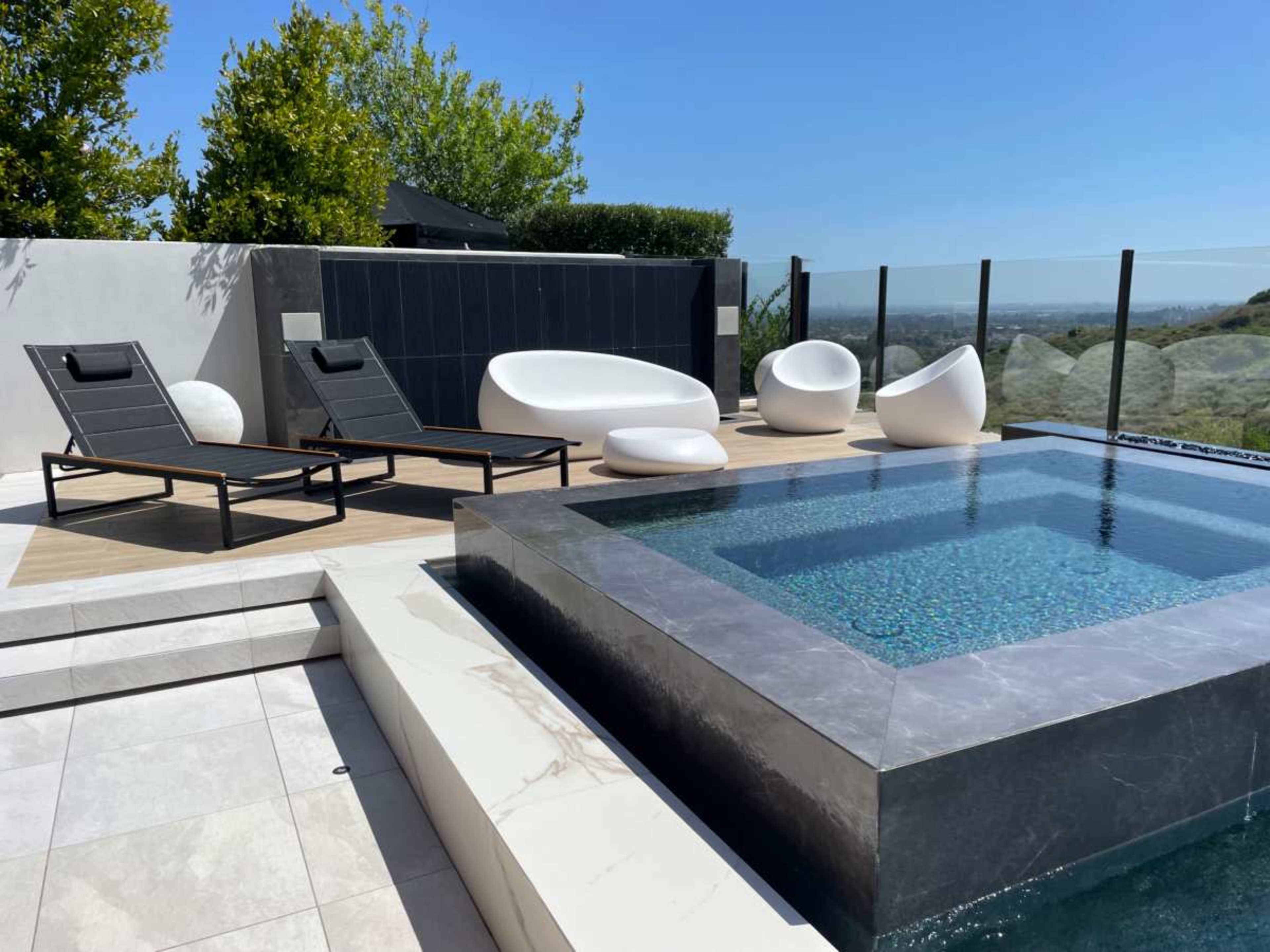 A modern outdoor area featuring a pool, lounge chairs, and sleek white furniture against a clear blue sky.