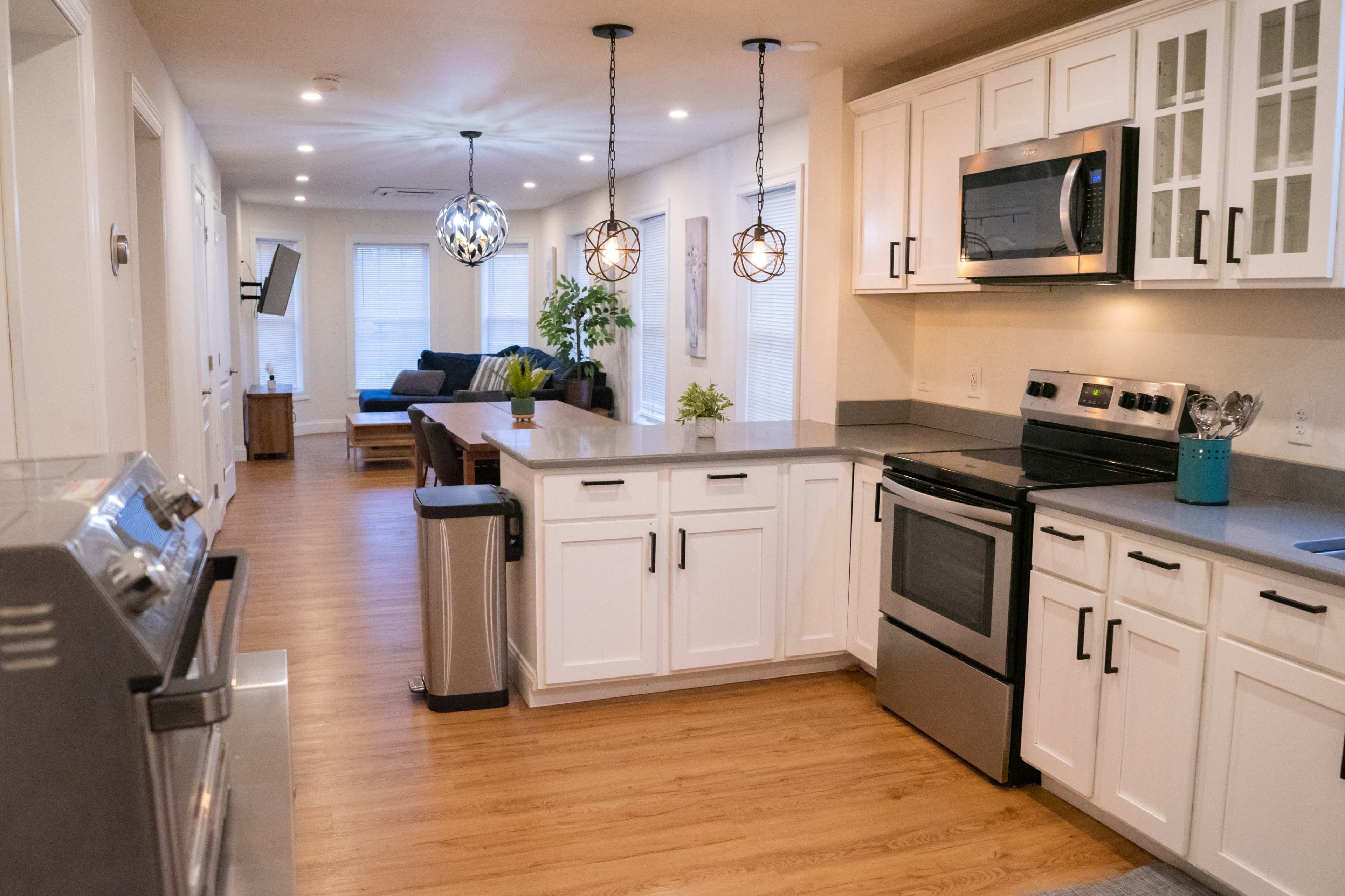A modern kitchen with white cabinetry, stainless steel appliances, and a countertop that opens to a living area with a sofa and a dining table.