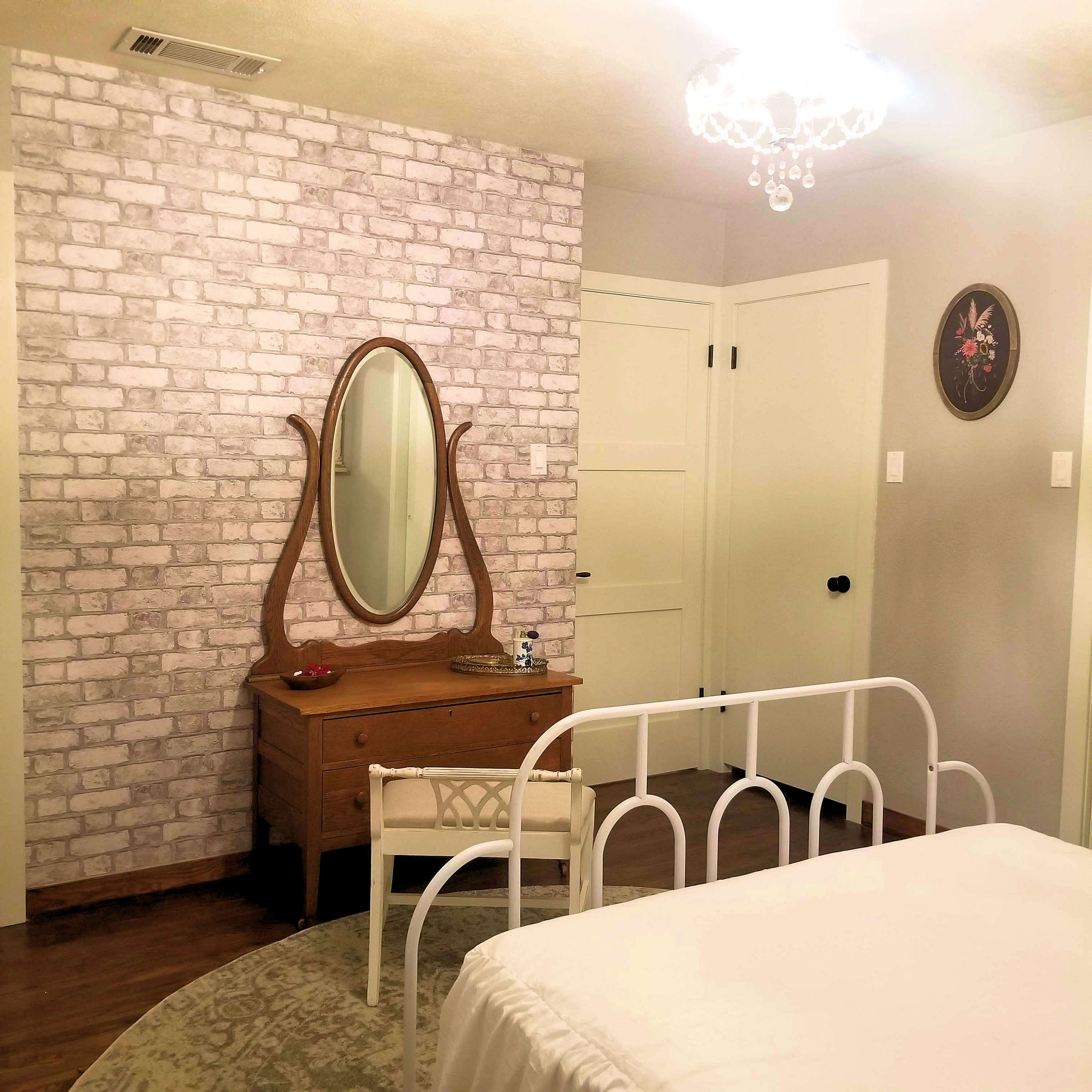 A bedroom featuring a white metal bed frame, a wooden dresser with a mirror, and a patterned accent wall.