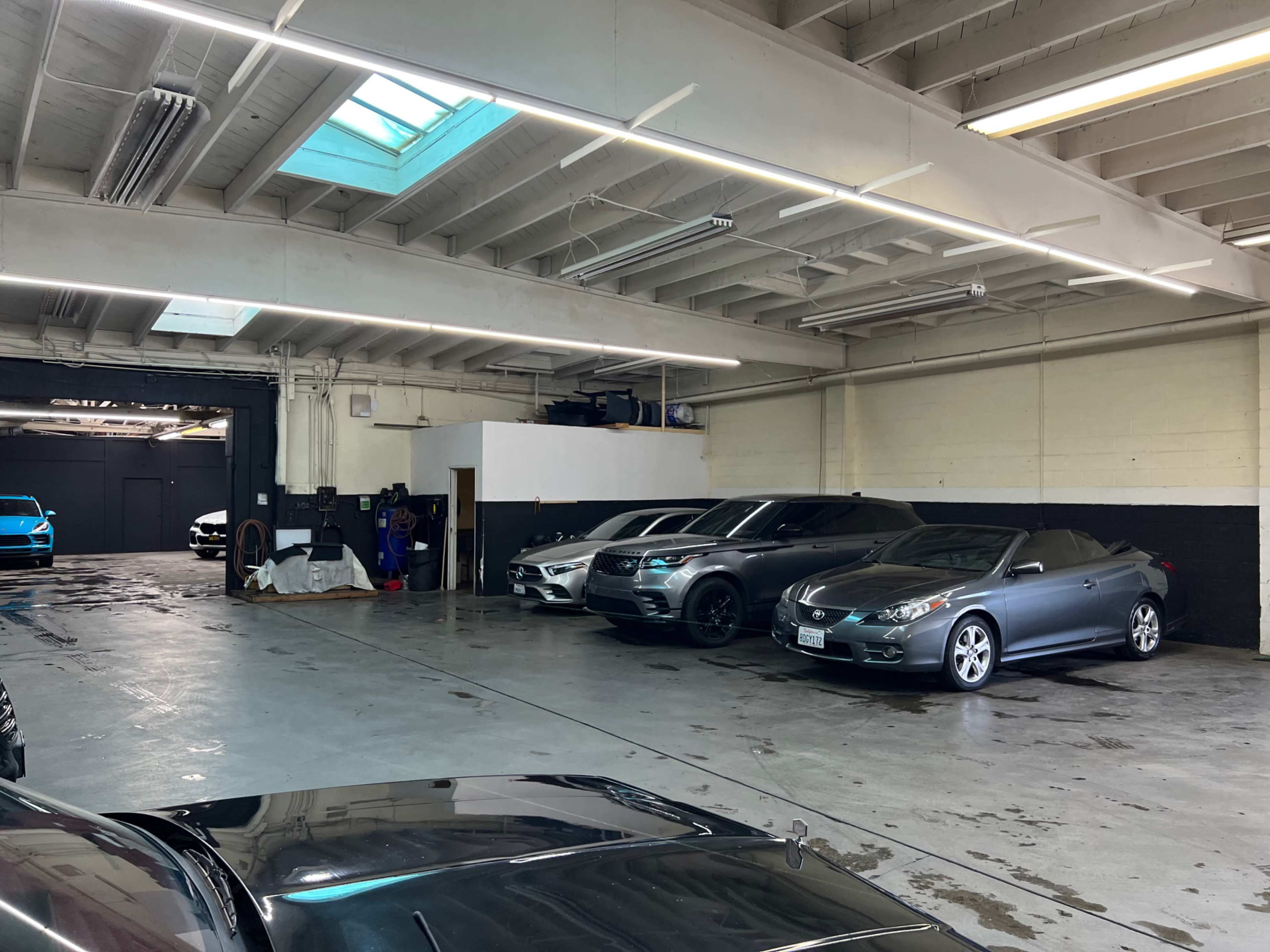 The image shows a spacious indoor parking area with several parked cars lined up along the walls.