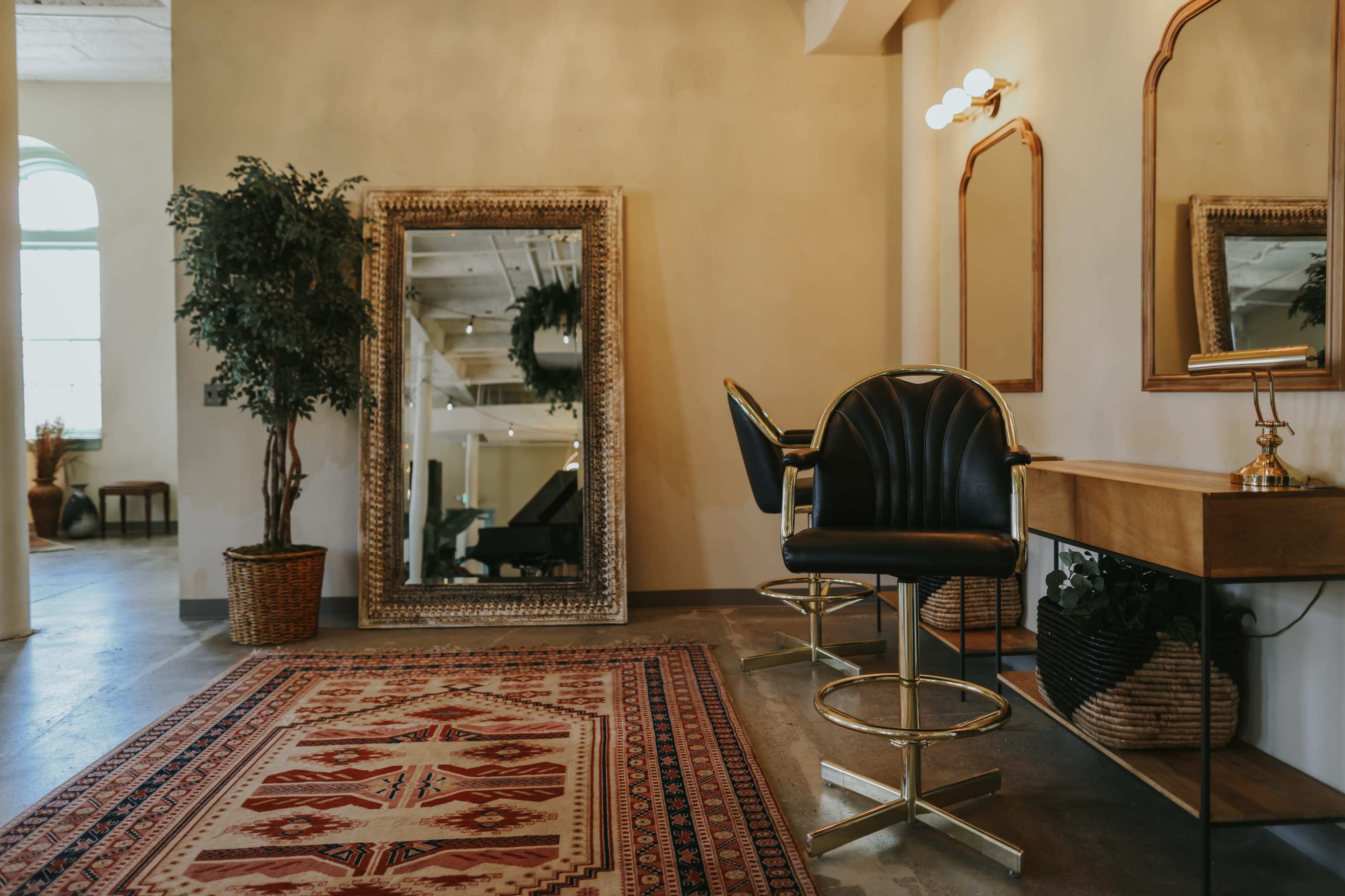 The image shows a salon interior featuring two black bar stools, a large decorative mirror, and a patterned area rug.