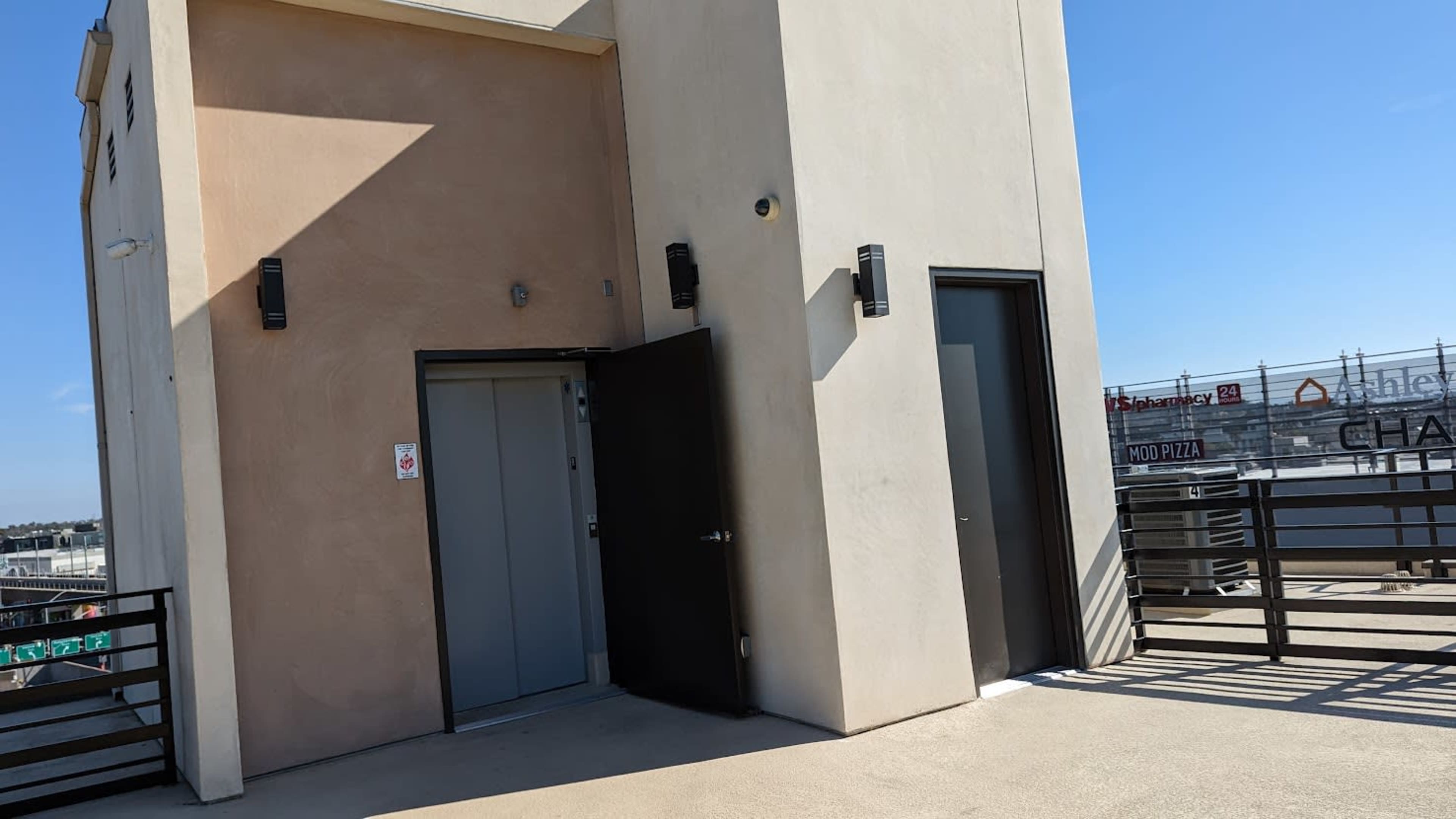 The image shows a rooftop area with two doors on a building, one door open and the other closed, under clear blue skies.