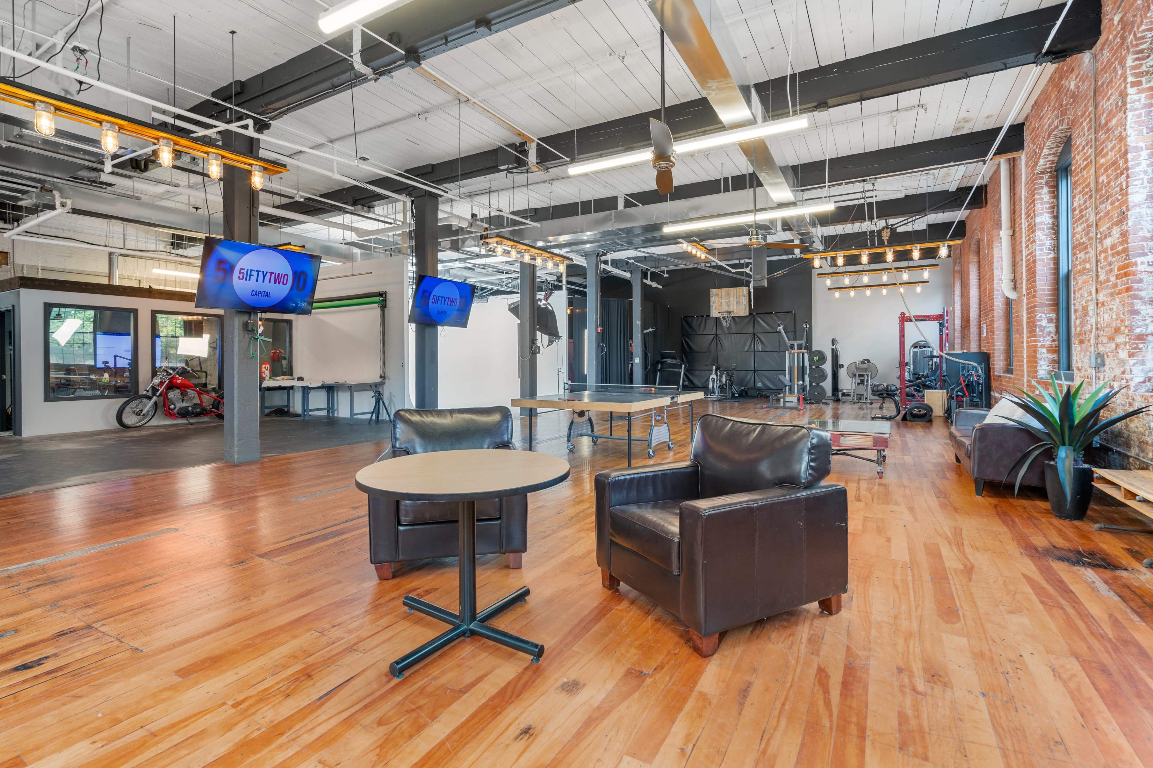 A spacious, modern interior with wooden flooring, two chairs, and large screens displaying fitness-related information.