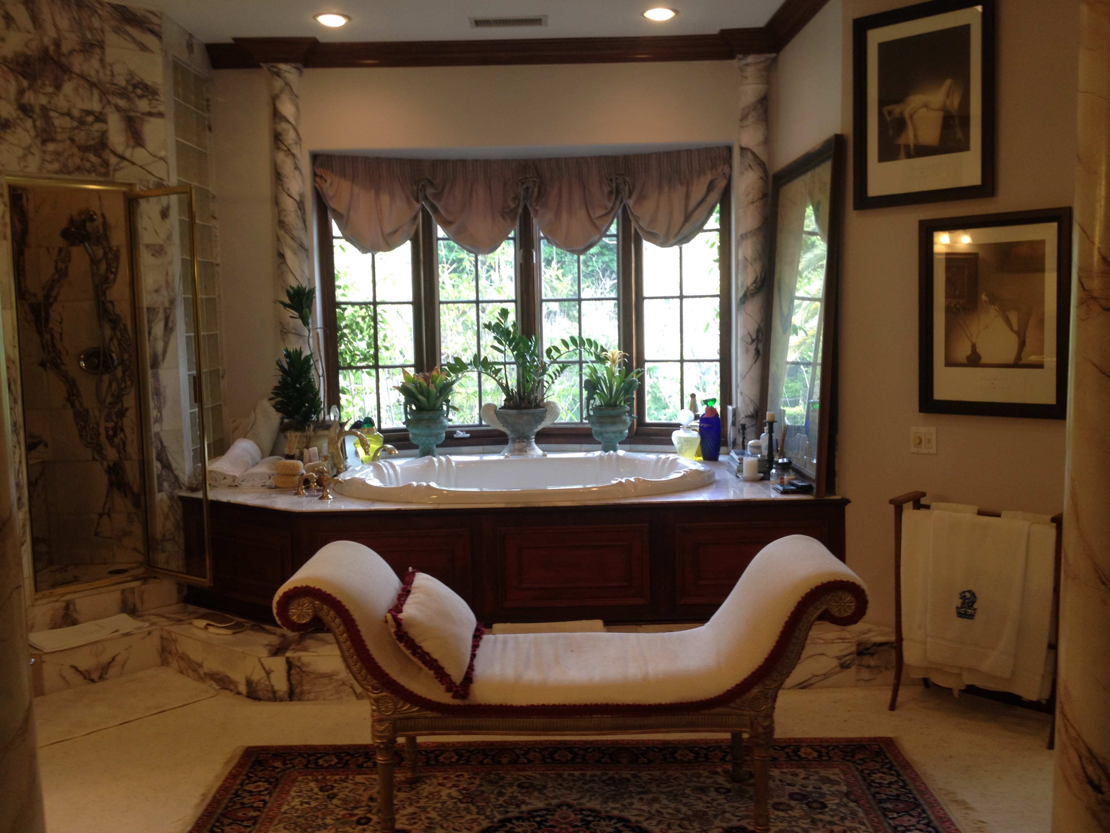 A spacious bathroom featuring a large bathtub surrounded by windows, ornate decor, and a chaise lounge.