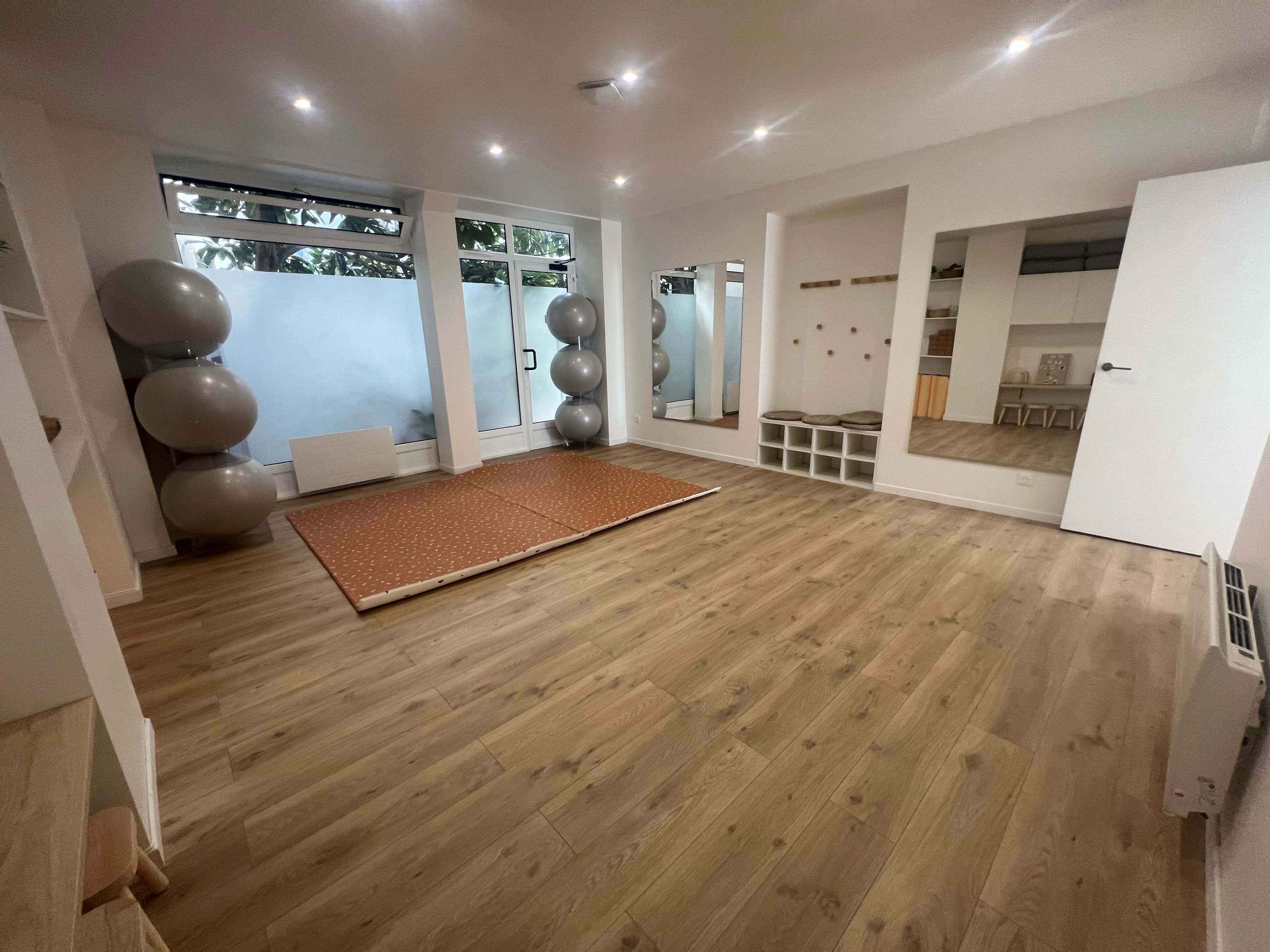 A spacious room with wooden flooring, large mirrors, exercise balls, and a patterned mat in the center.