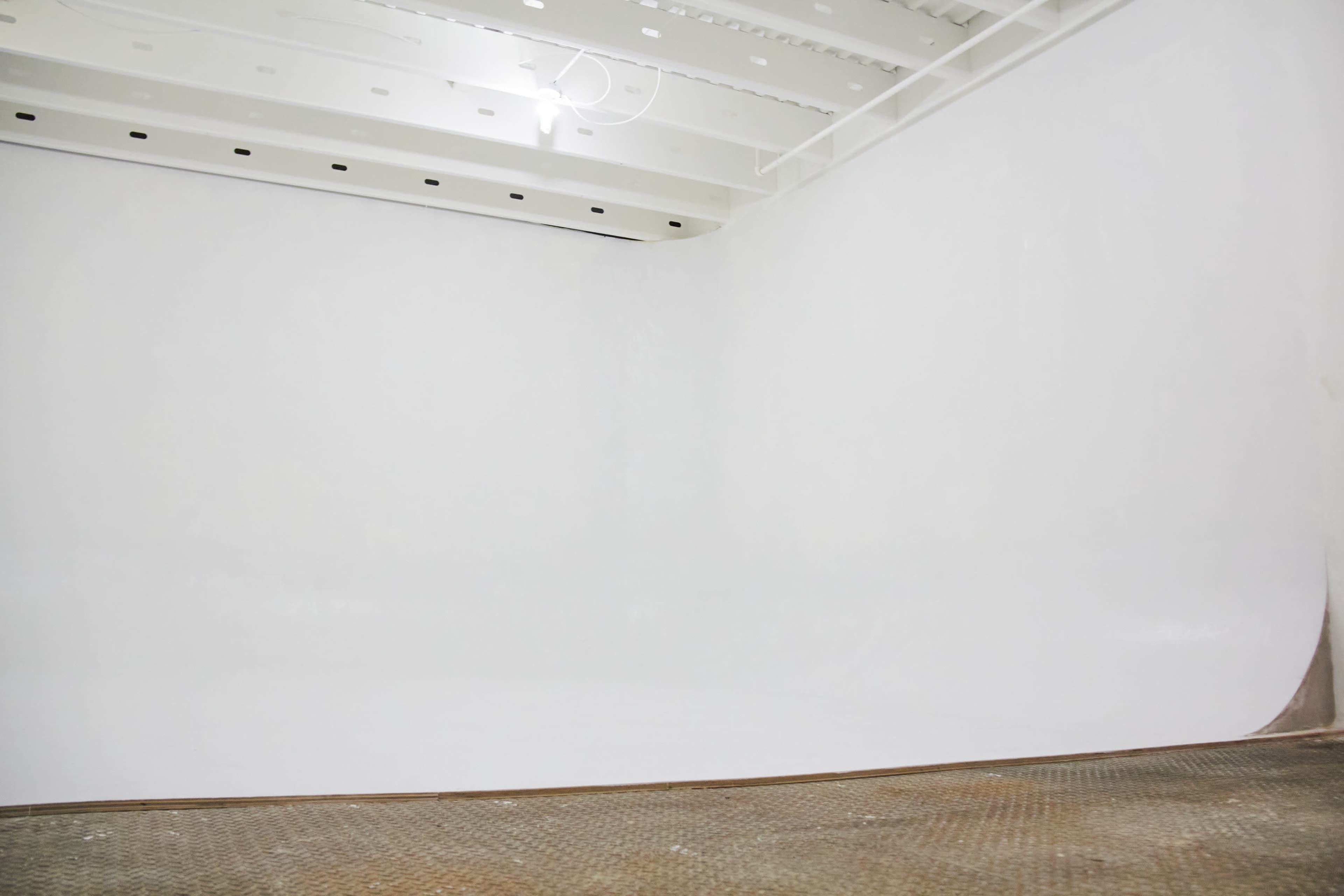 The image shows an empty room with a seamless white background and a concrete floor.