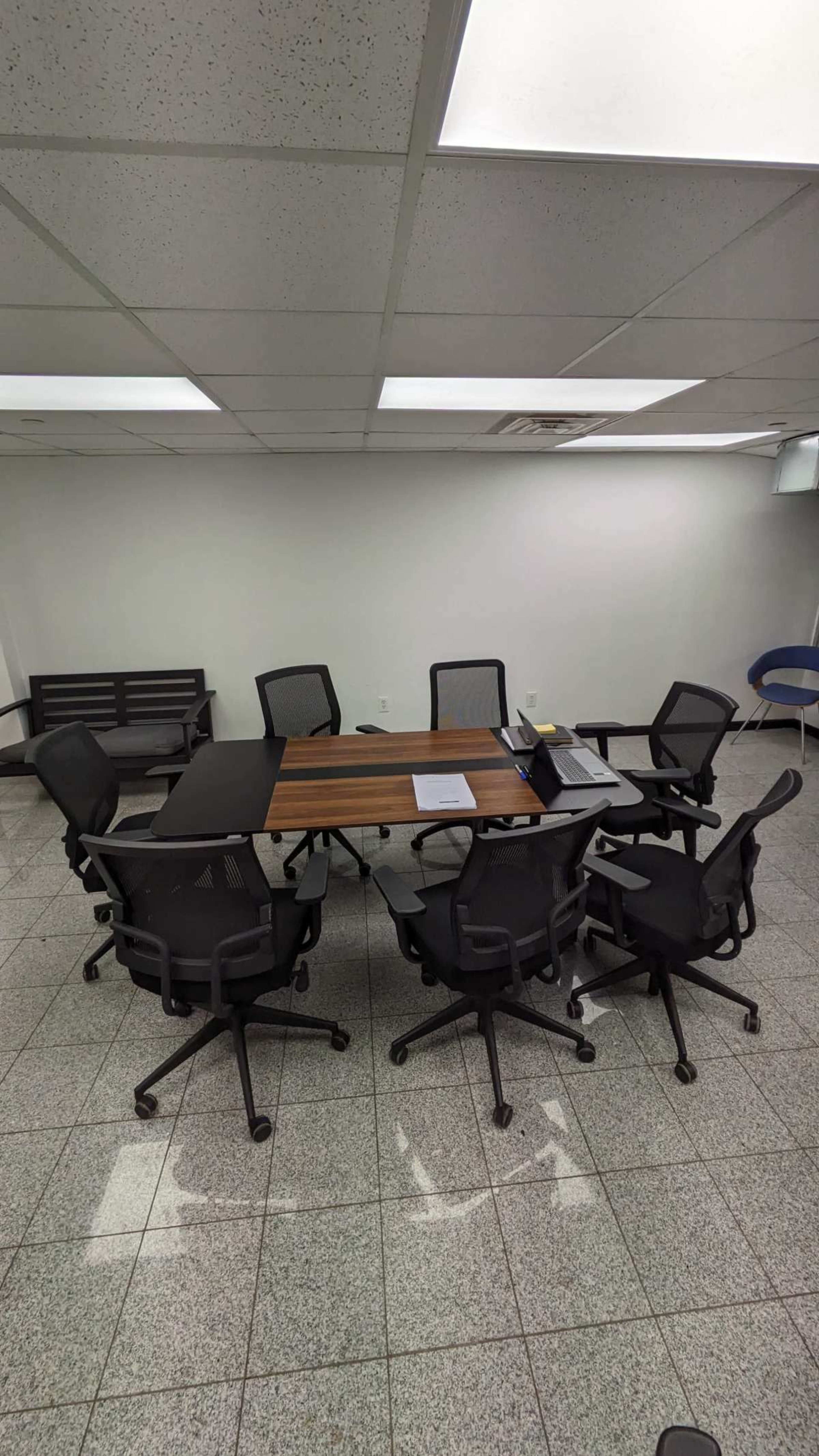 A conference room with a rectangular table surrounded by black office chairs on a tiled floor.