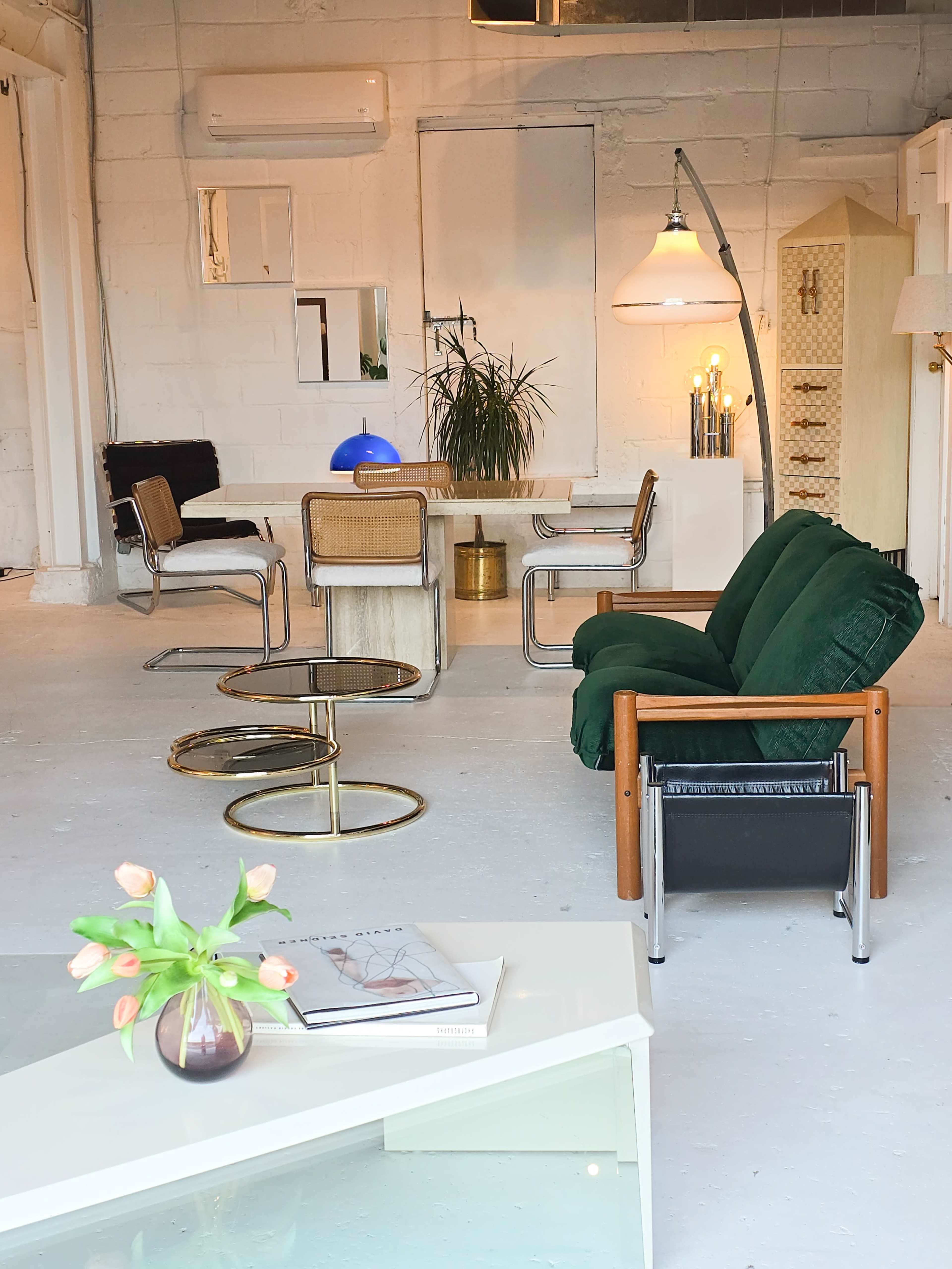 The image shows a minimalist interior space featuring a green sofa, a glass coffee table, a dining table with chairs, and various decorative items.