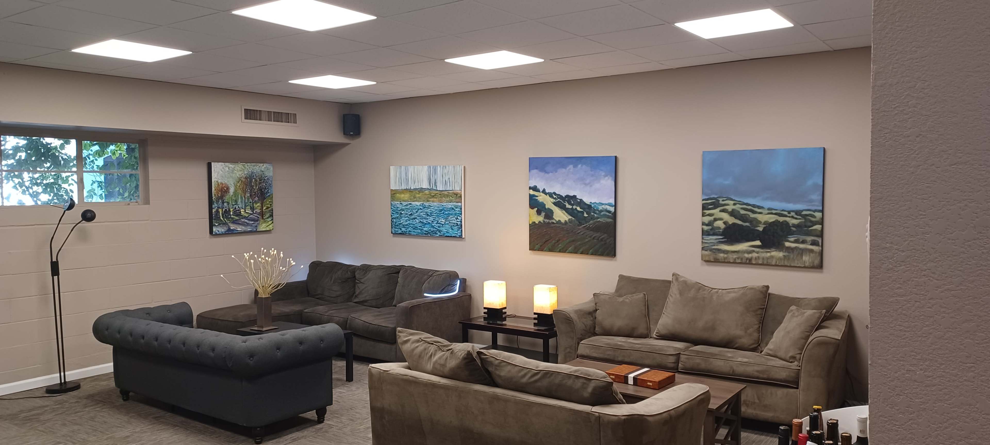 The image shows a cozy indoor seating area with two sofas, coffee tables, and several paintings displayed on the walls.