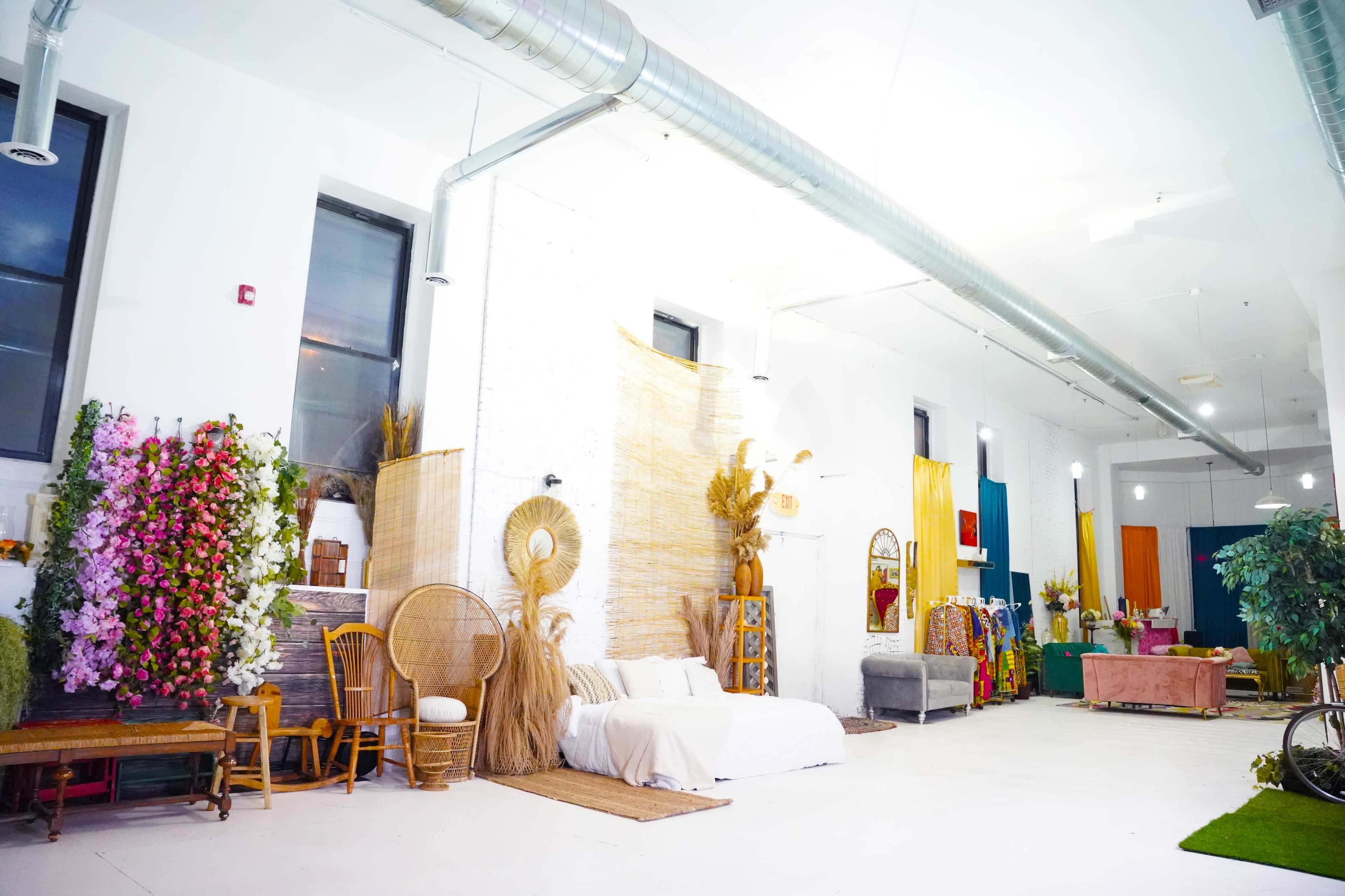 A spacious indoor setting with a bed, decorative plants, a woven wall, and various seating arrangements.