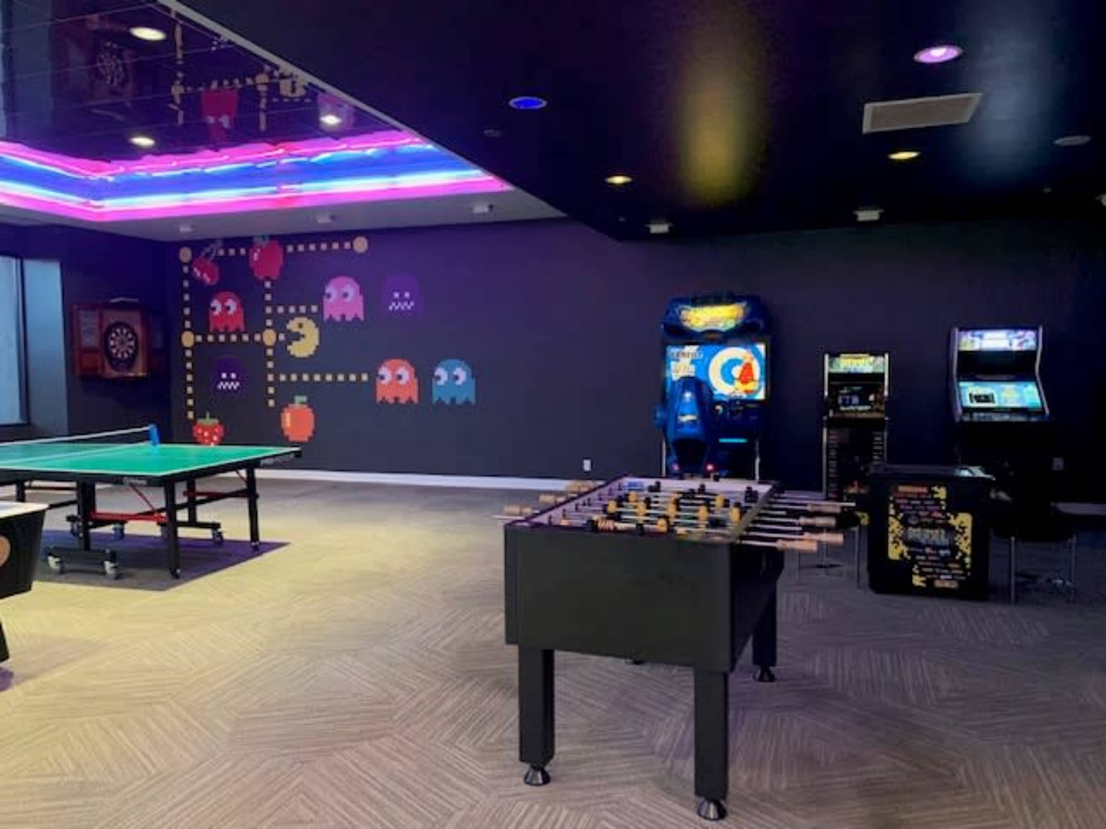 A game room with a foosball table, a pool table, an arcade machine, and vibrant wall decorations featuring pixelated characters.