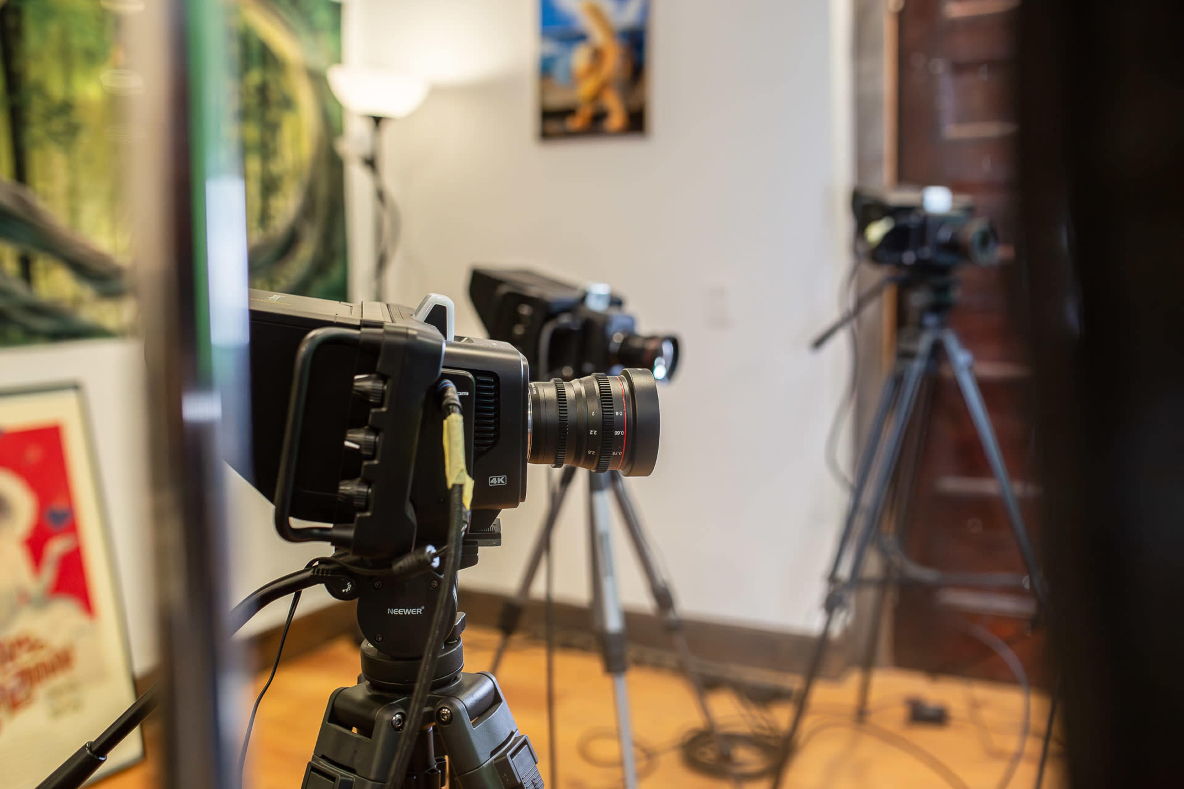 The image shows several cameras on tripods set up in a room, with a softly lit background and various framed images on the walls.