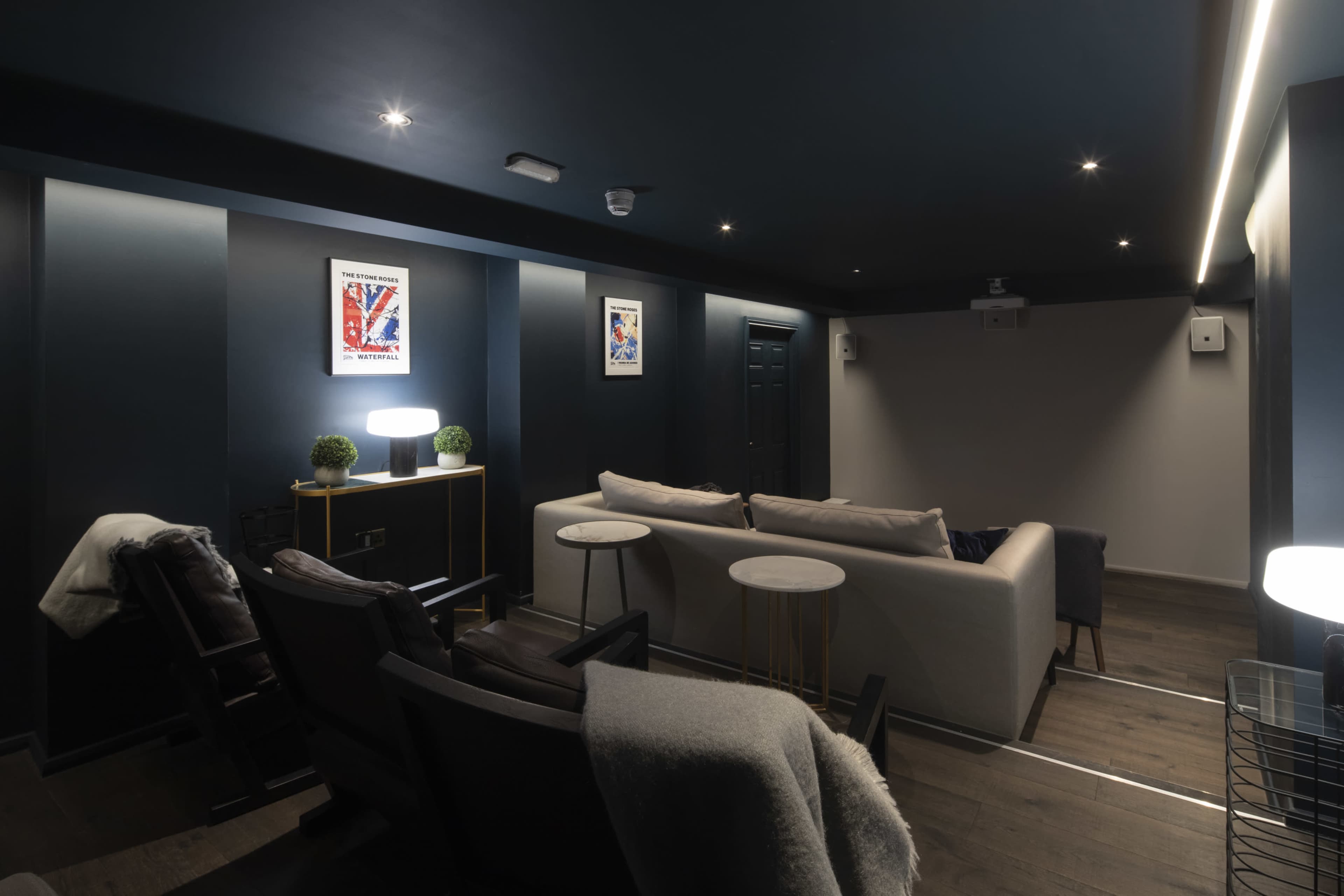 The image shows a modern home theater with dark walls, a projector, comfortable seating, and decorative art on the walls.