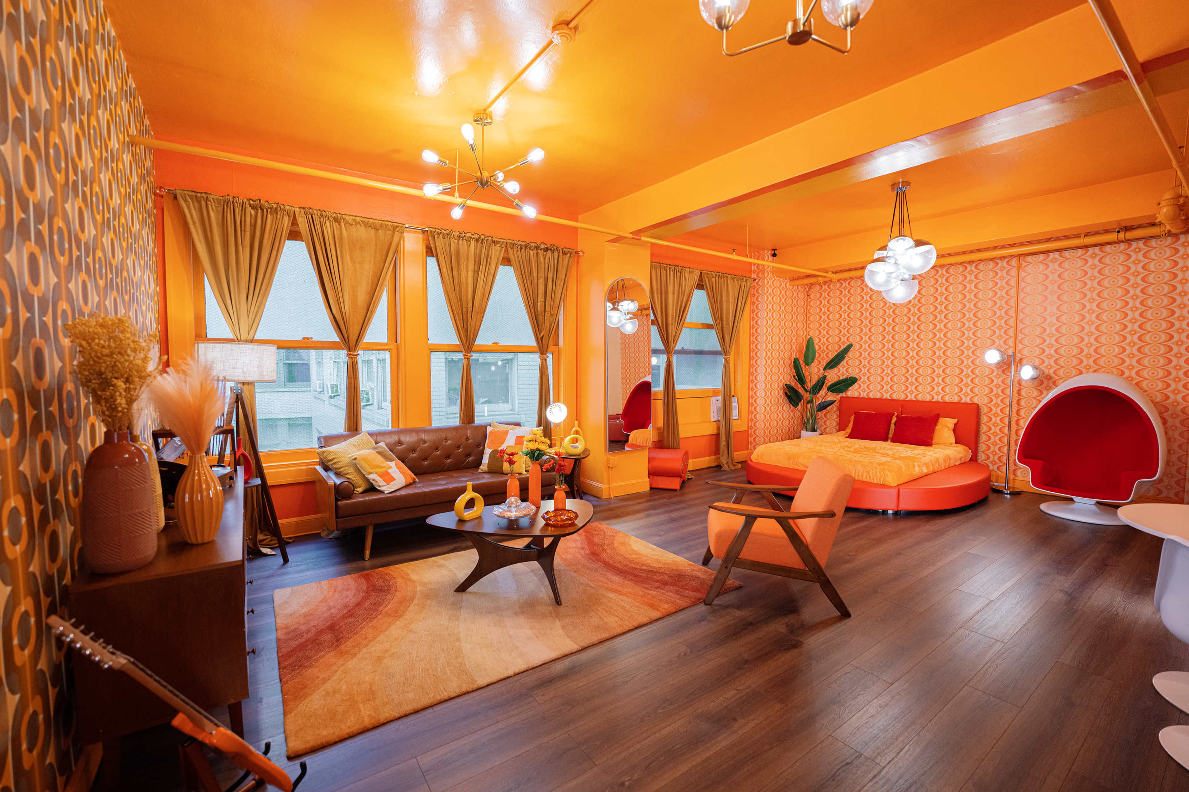A vibrant living room with orange walls, a circular red bed, a brown sofa, and retro decor elements.