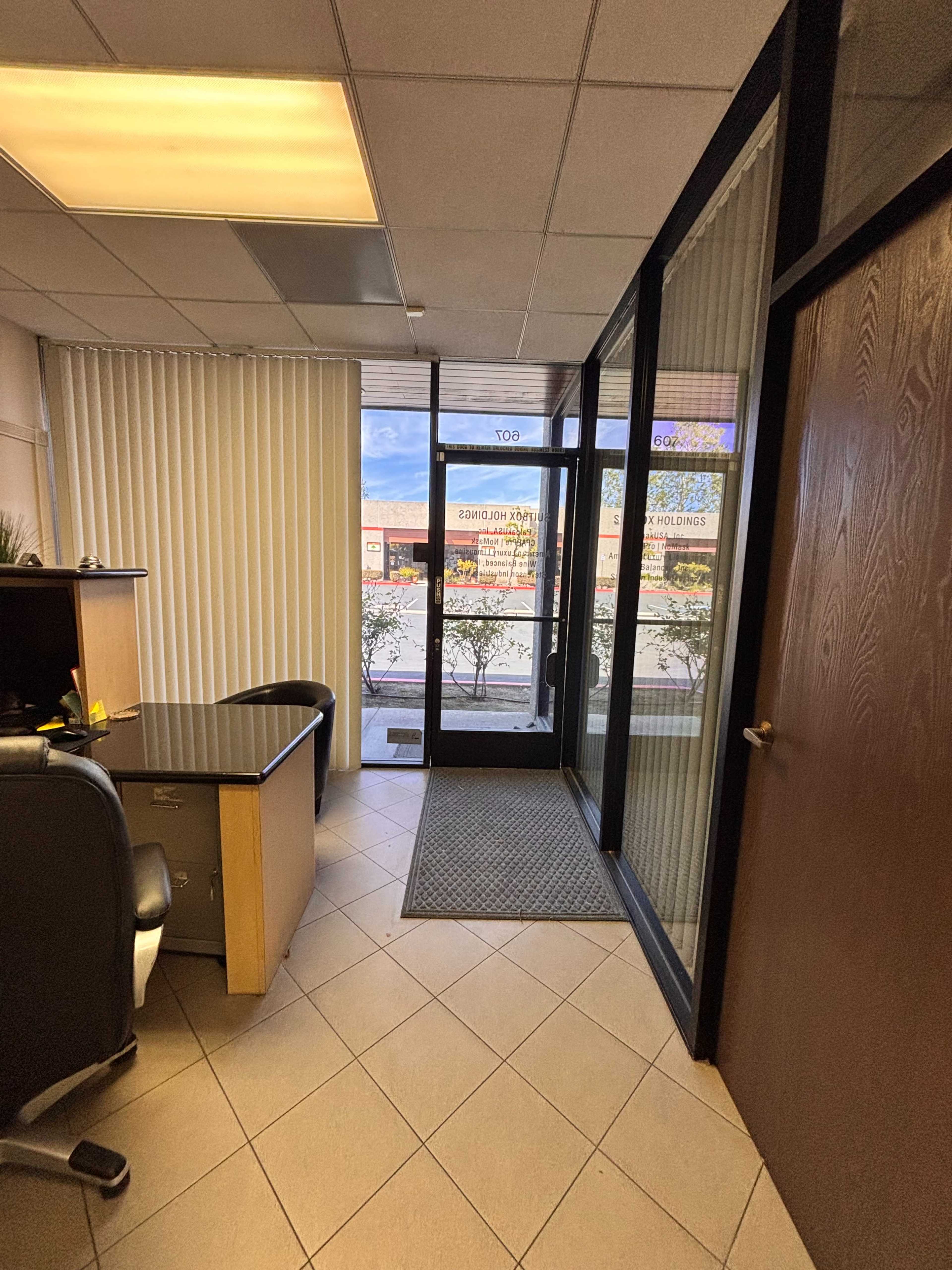 The image shows an office space with a desk and black chair, leading to a glass door that opens to an exterior view with signage.