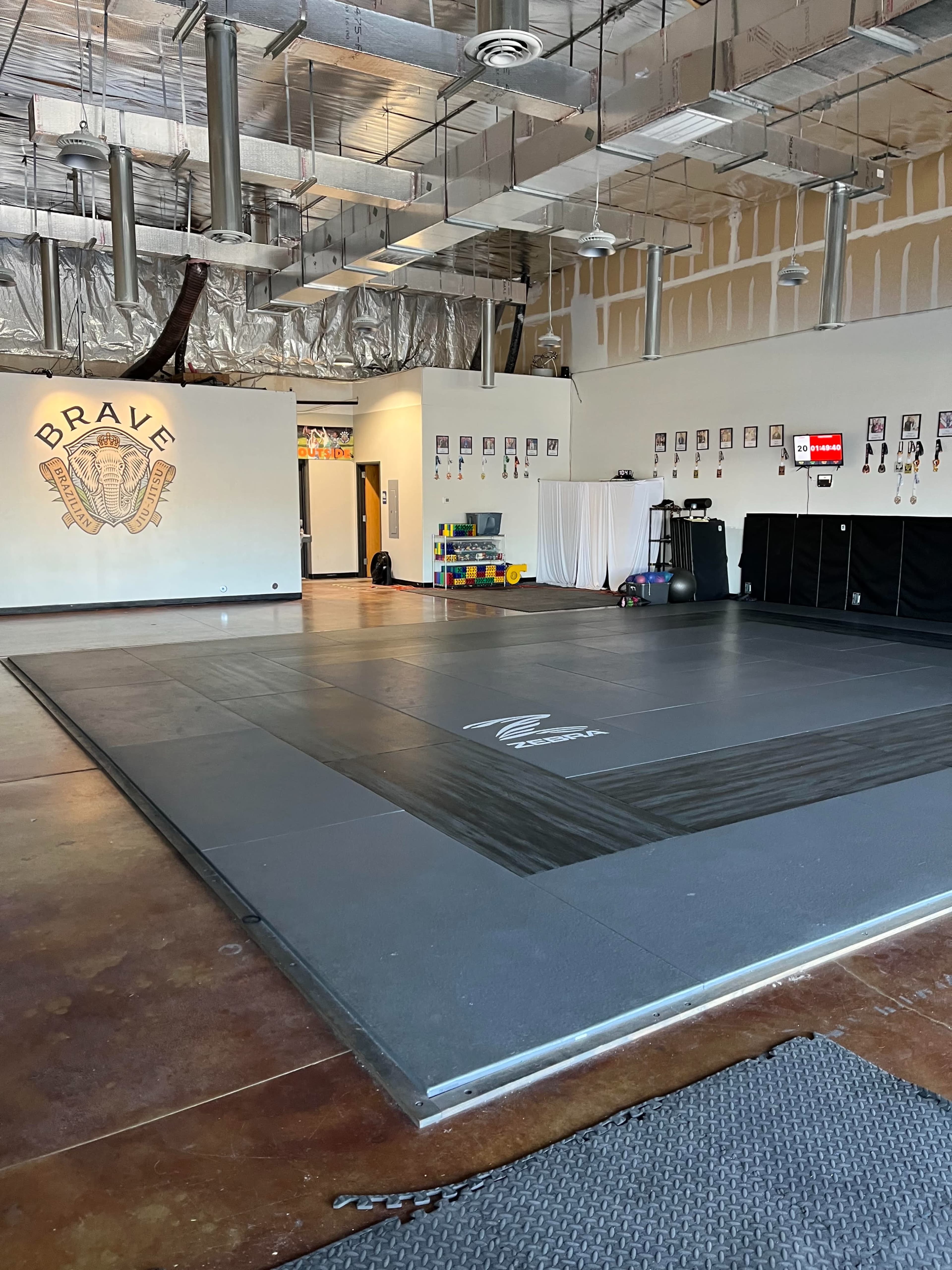 The image shows an empty martial arts training studio with a black mat in the center, surrounded by walls featuring various decorations and a small area with colorful toys in the background.