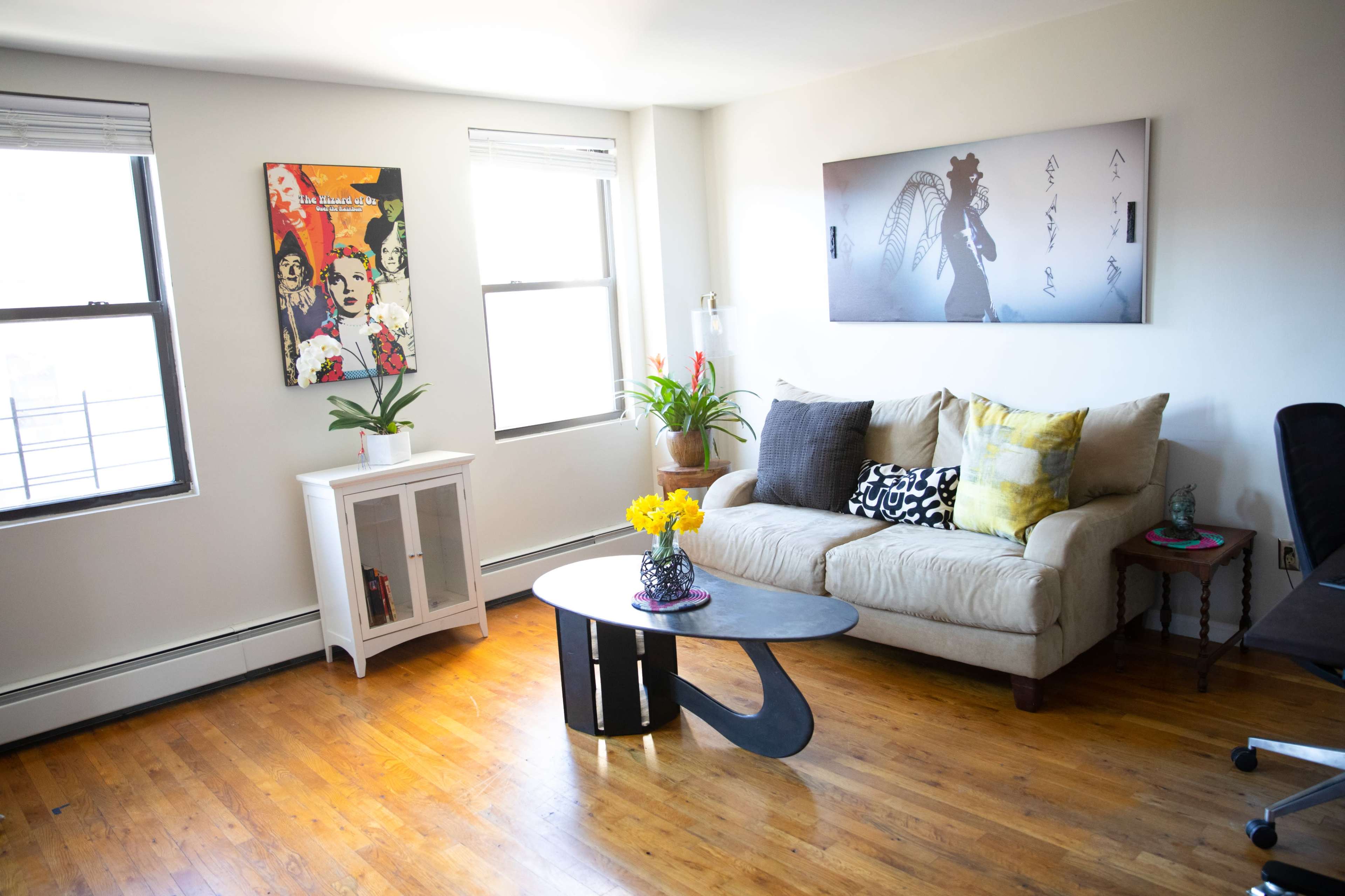 A well-lit living room with a beige couch, a coffee table, a white cabinet, and artwork on the walls.