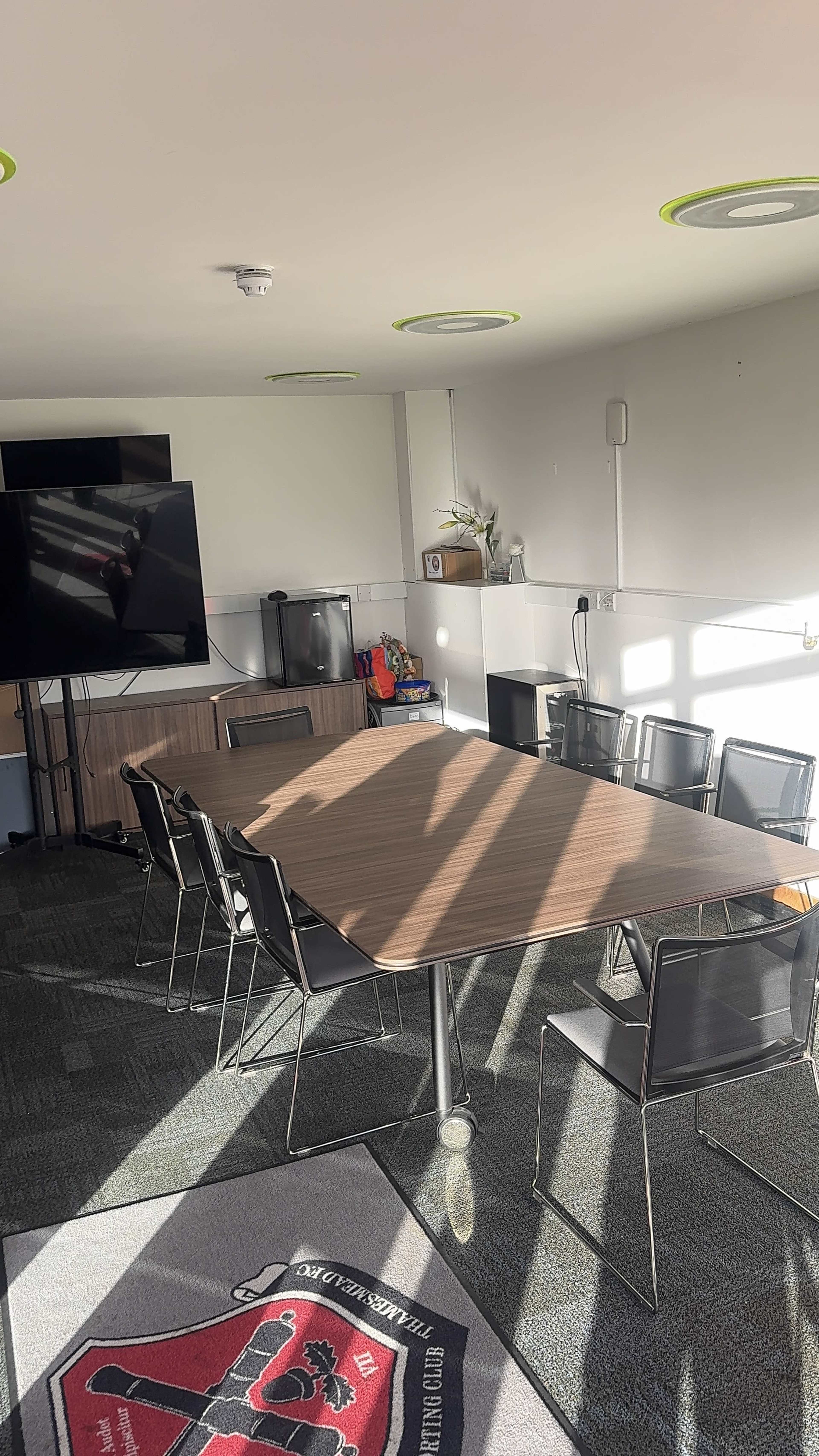 The image shows a modern conference room with a large table, several black chairs, and a television display along one wall.